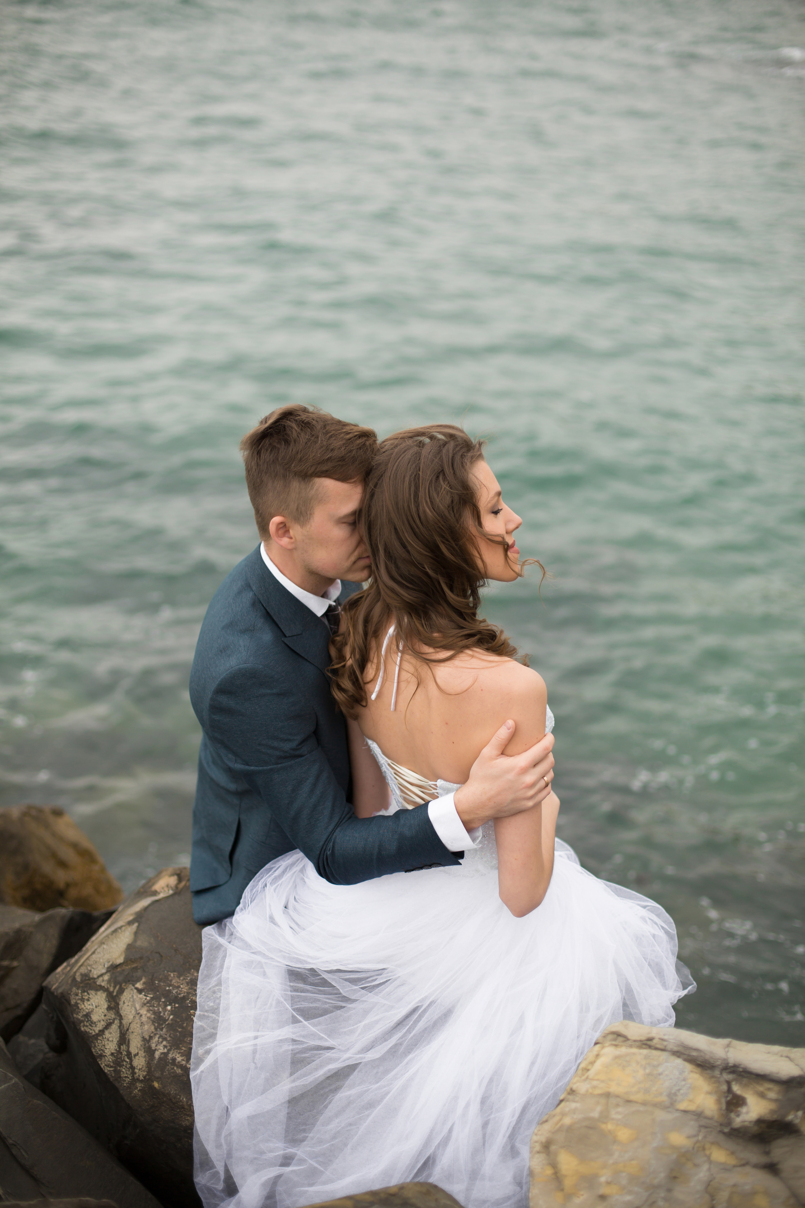 жених и невеста сидят спиной и смотрят на море