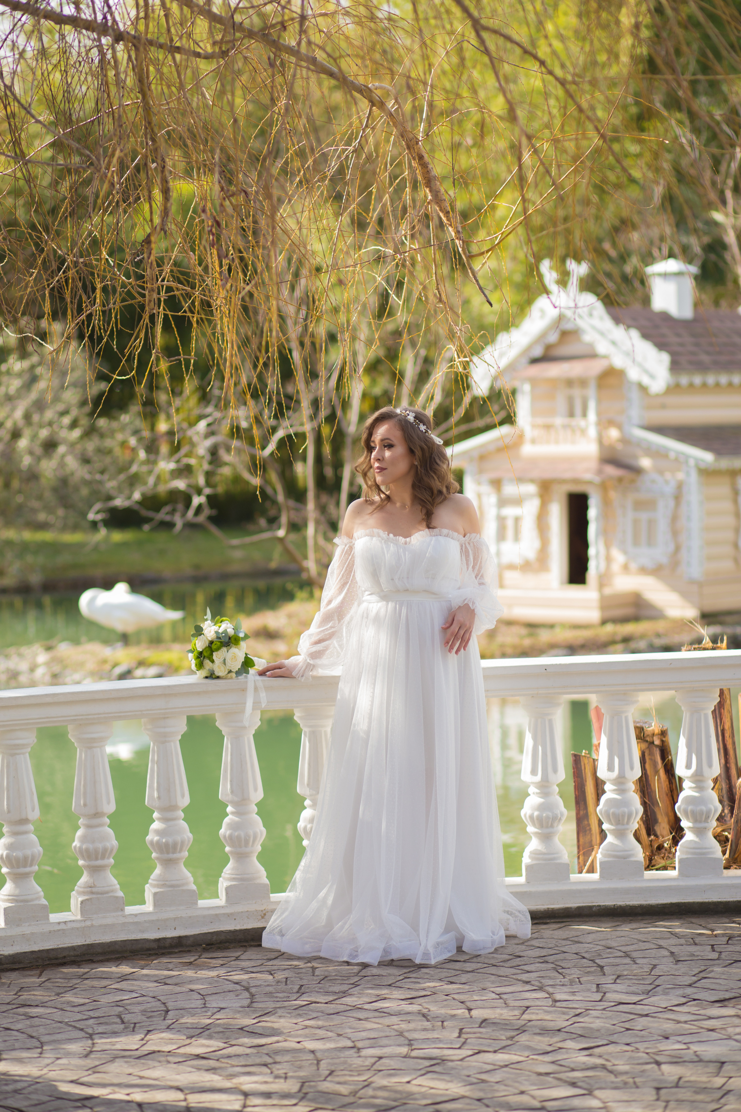 невеста в свадебном платье стоит на фоне домика и озера