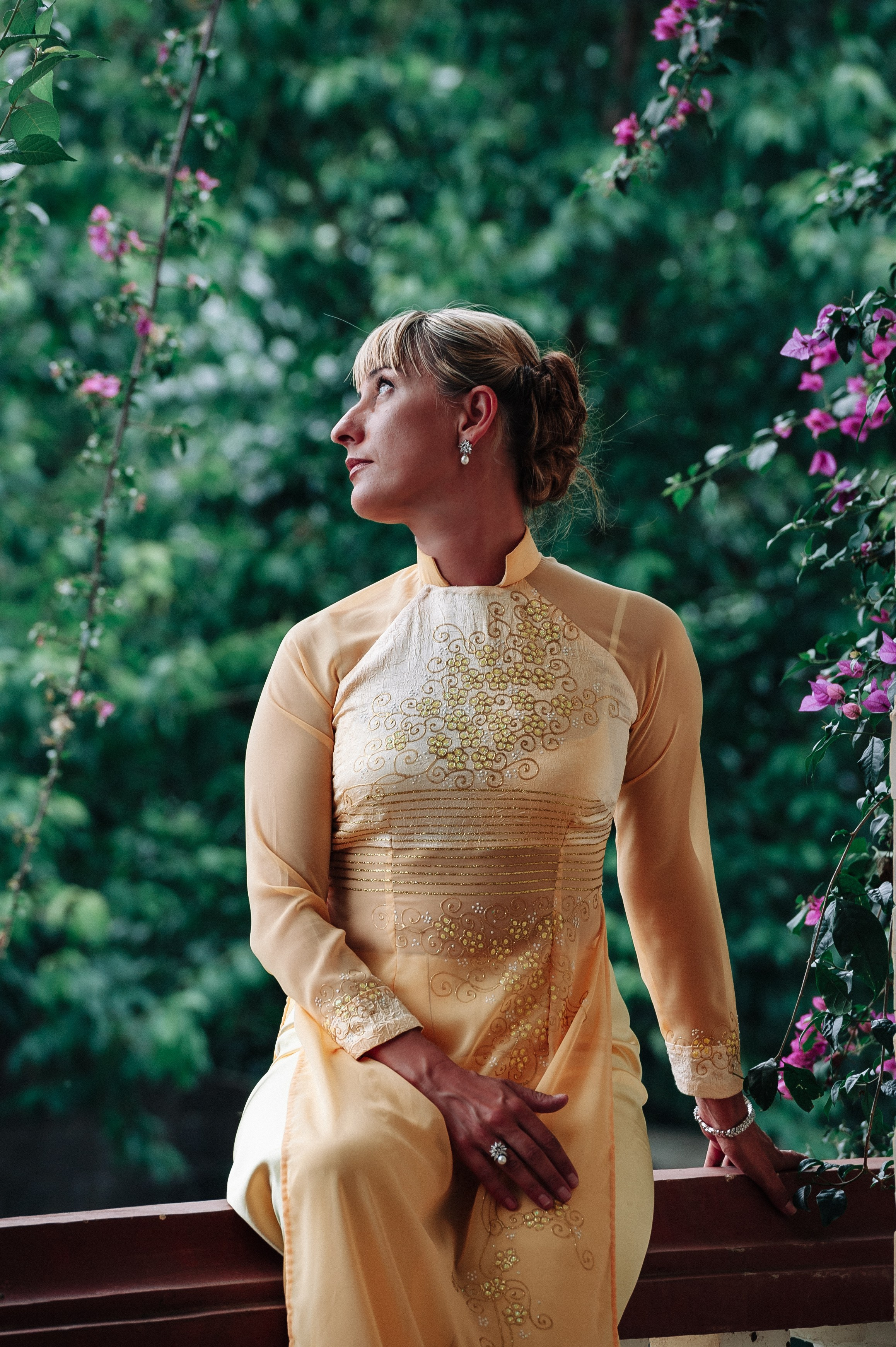 Фотосессия девушки в традиционном вьетнамском костюме Аозай золотого цвета, сидящей в саду