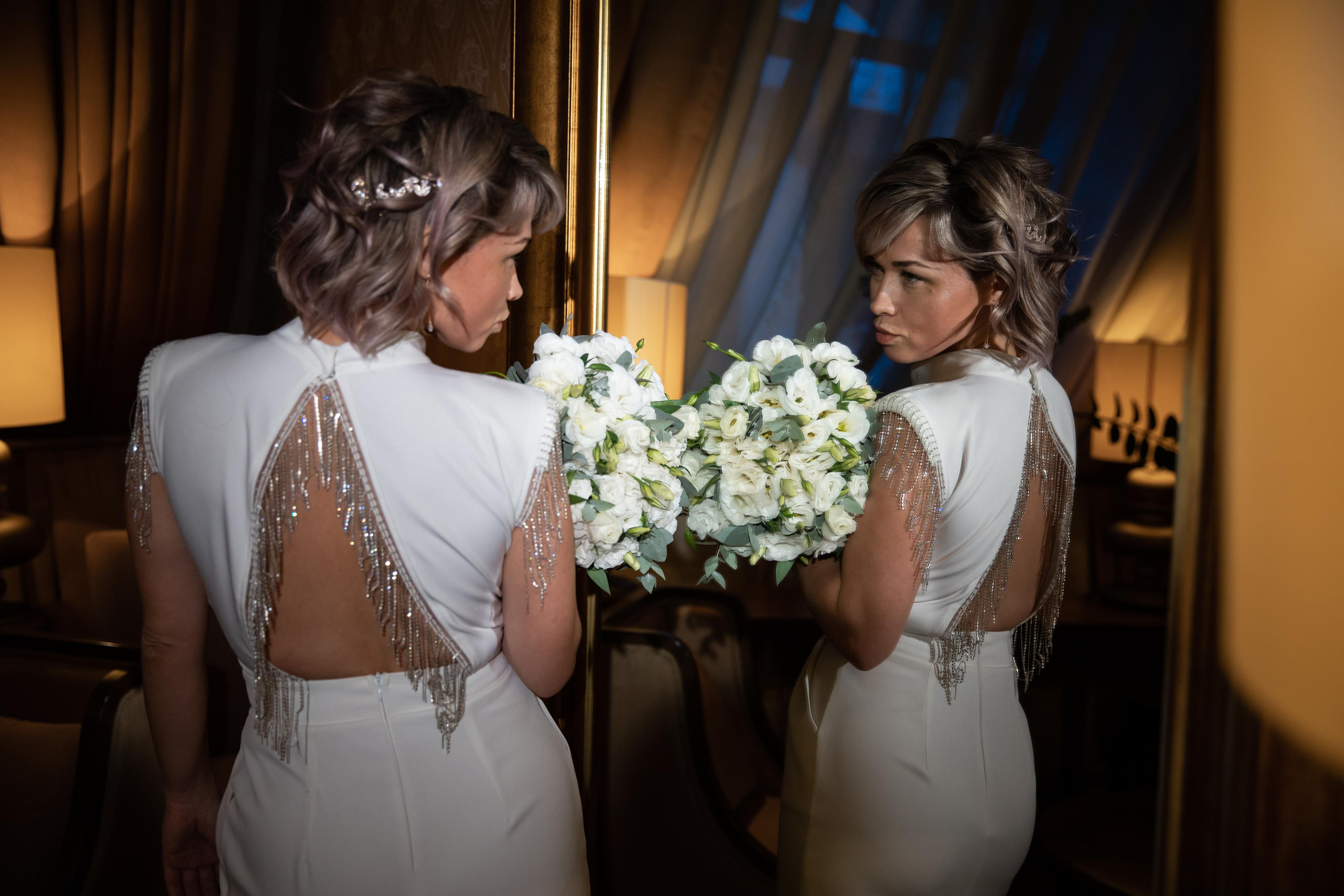невеста с букетом стоит у зеркала