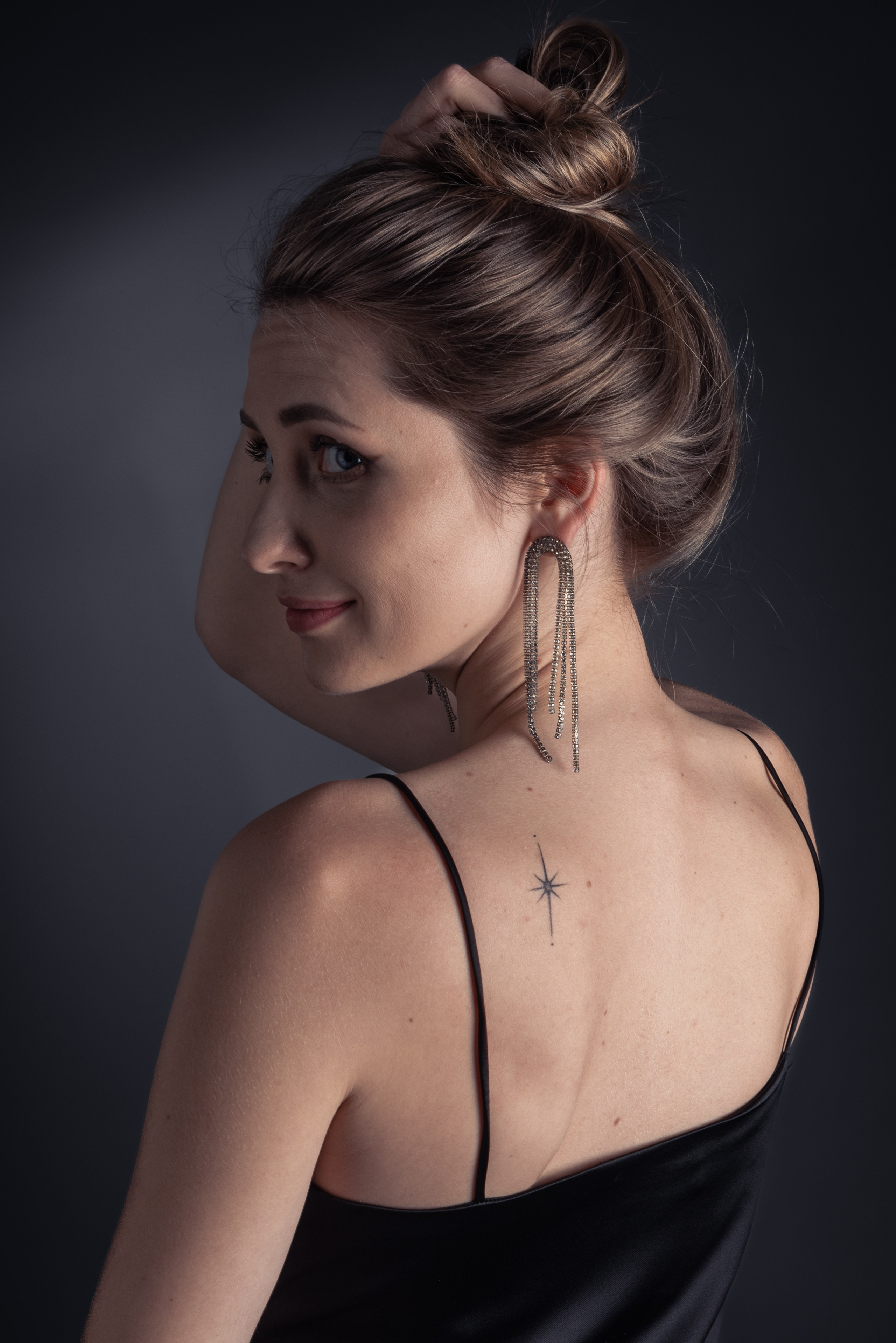 Фото в студии. Девушка стоит спиной, оглядывается через плечо, улыбается.