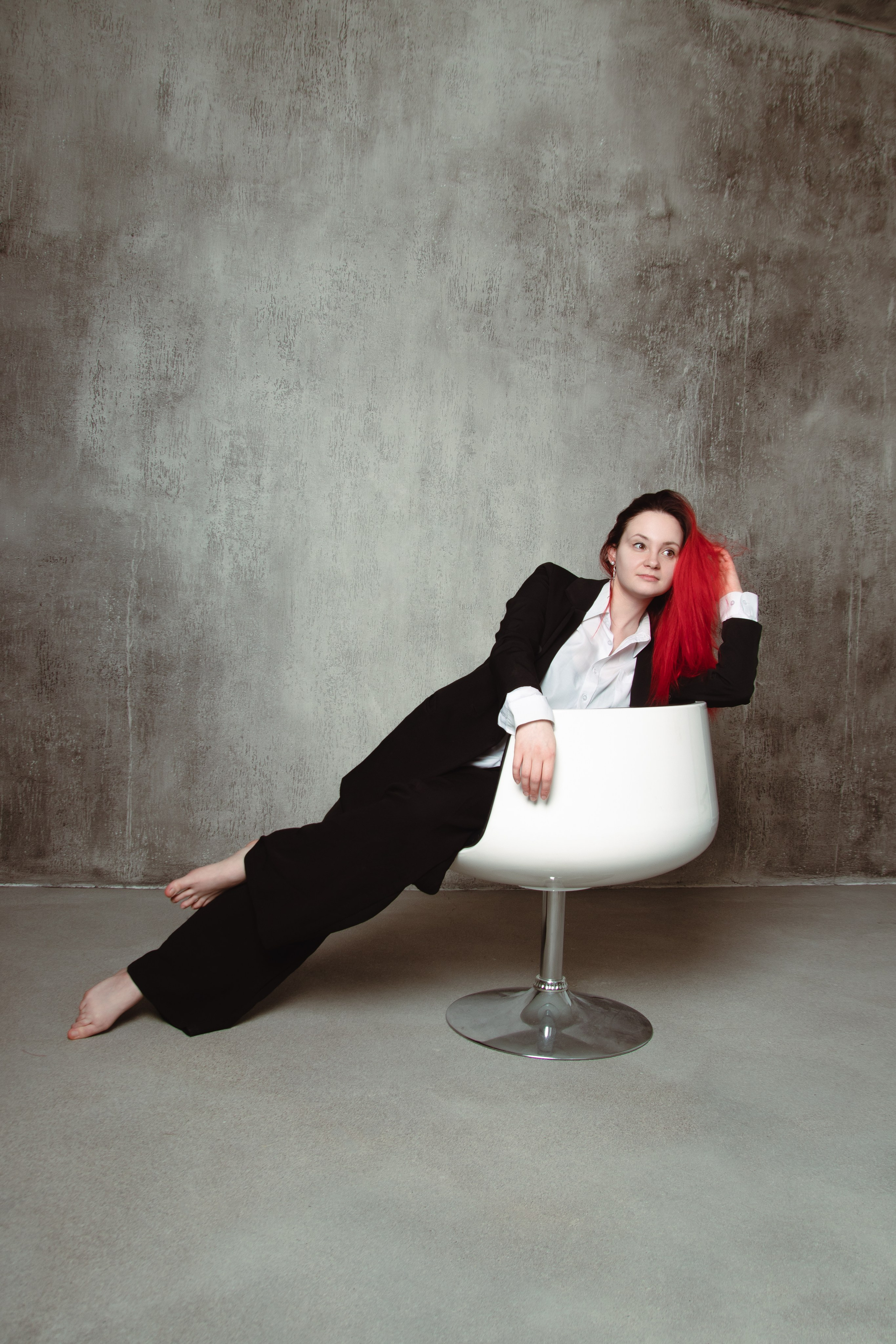 Девушка с красными волосами на белом стуле на светлом фоне в классическом костюме