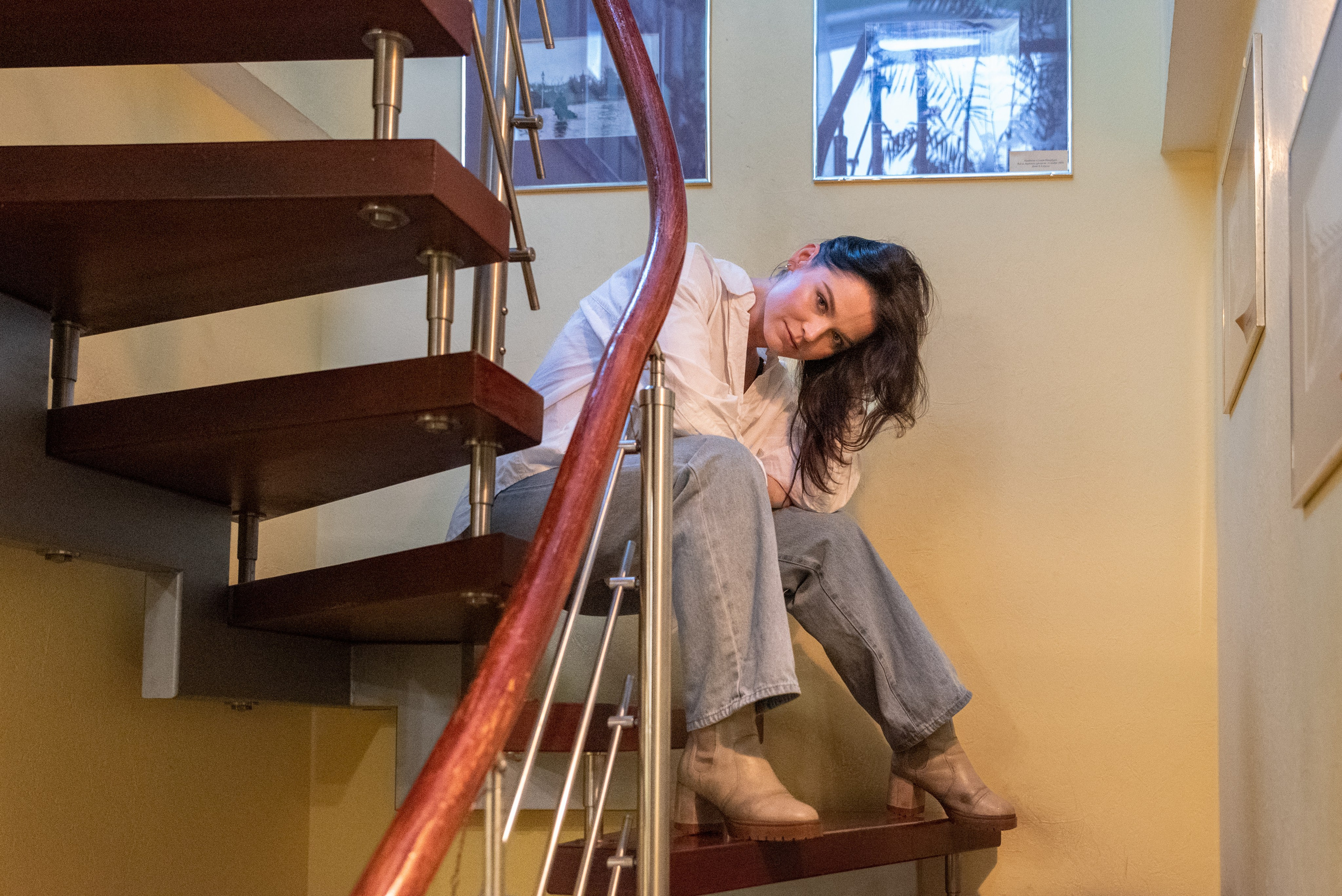 Девушка сидит на винтовой лестнице, наклонила голову, смотрит в камеру