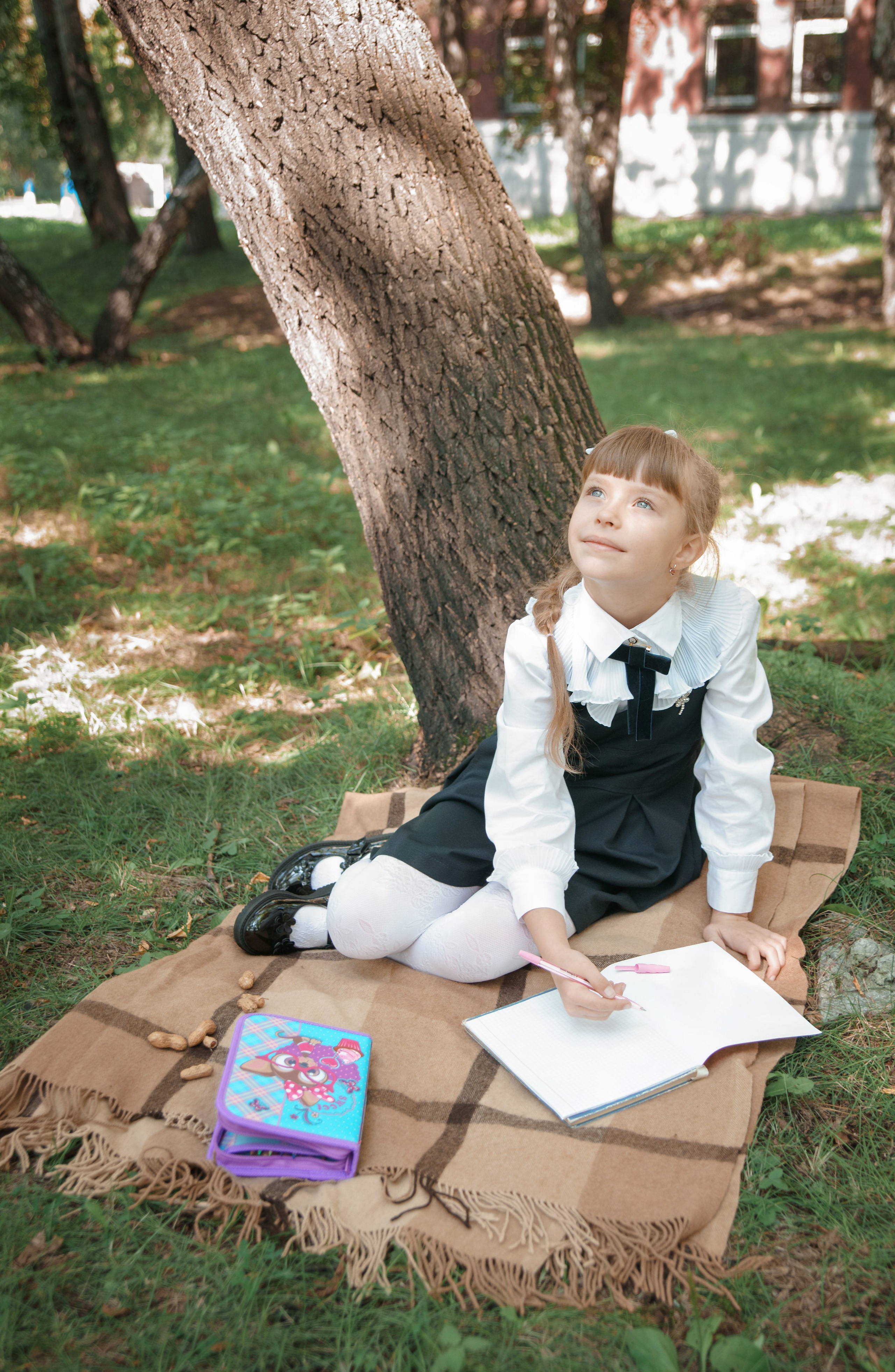 Детская фотосессия осенью - школьница сидя у дерева смотрит вверх