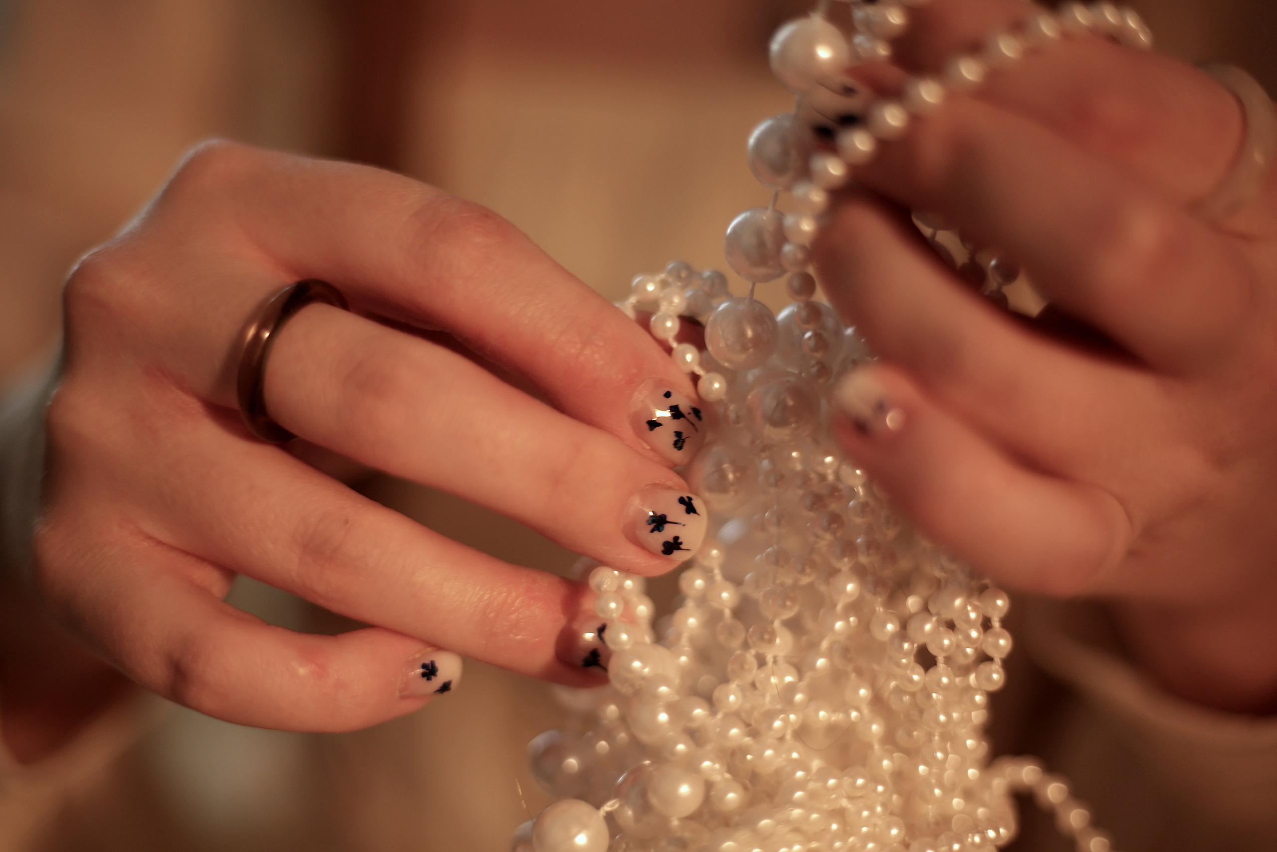 Детали фентезийной фотосессии: руки девушки с аккуратным маникюром, держащие нить жемчужин