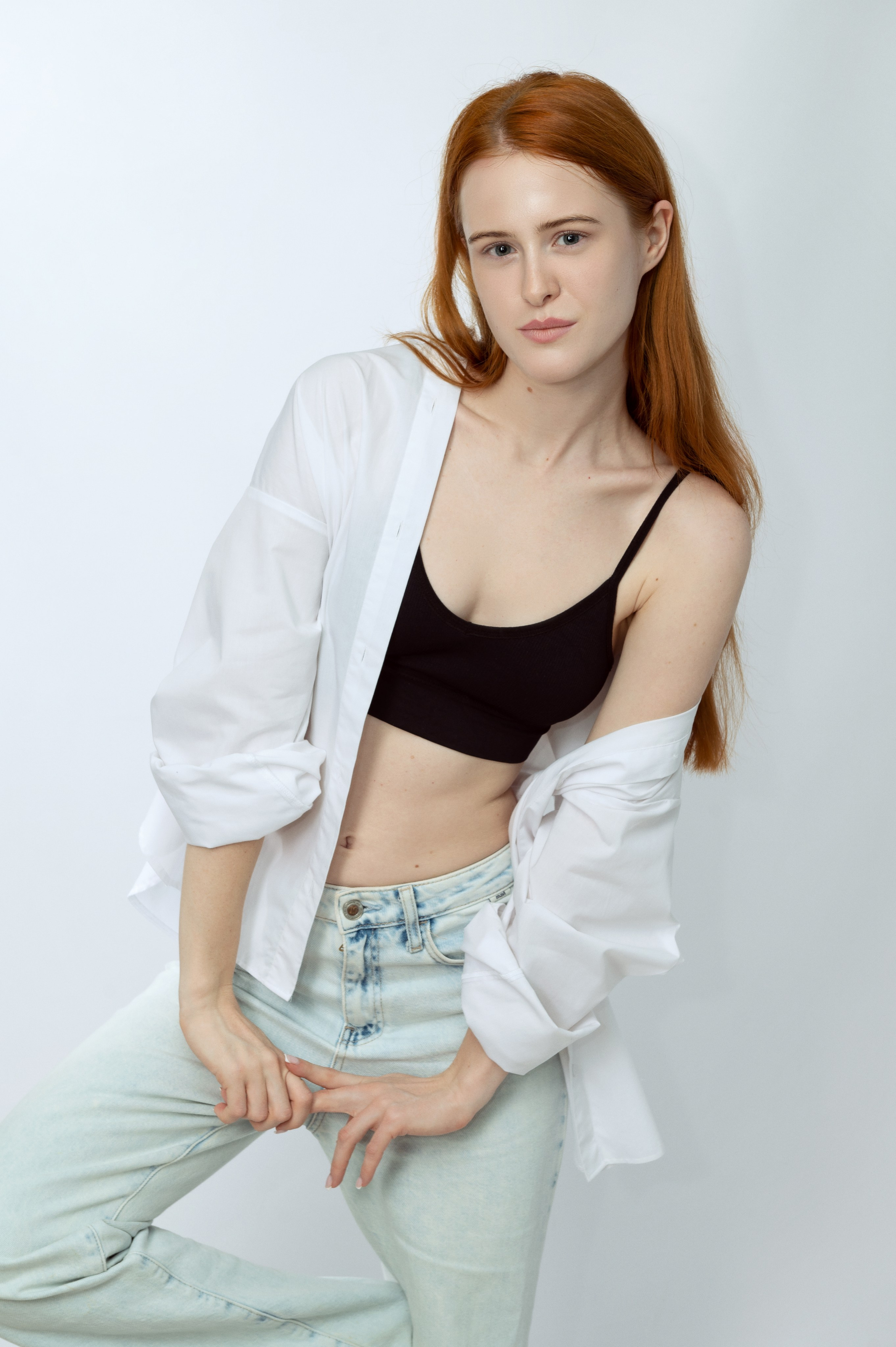 Рыжеволосая девушка-модель в белой рубашке и светлых джинсах на светлом фоне. Модельные тесты