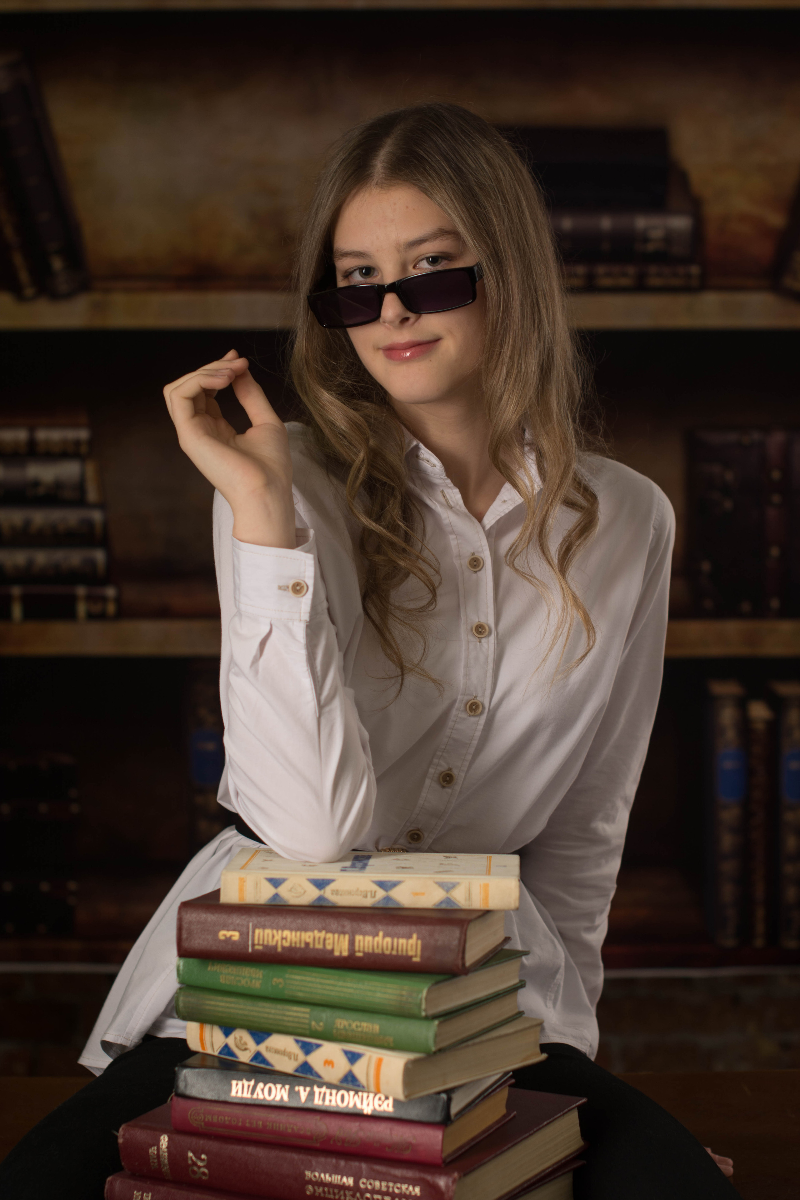 Симпатичная девочка из 10 класса позирует в очках в библиотеке.