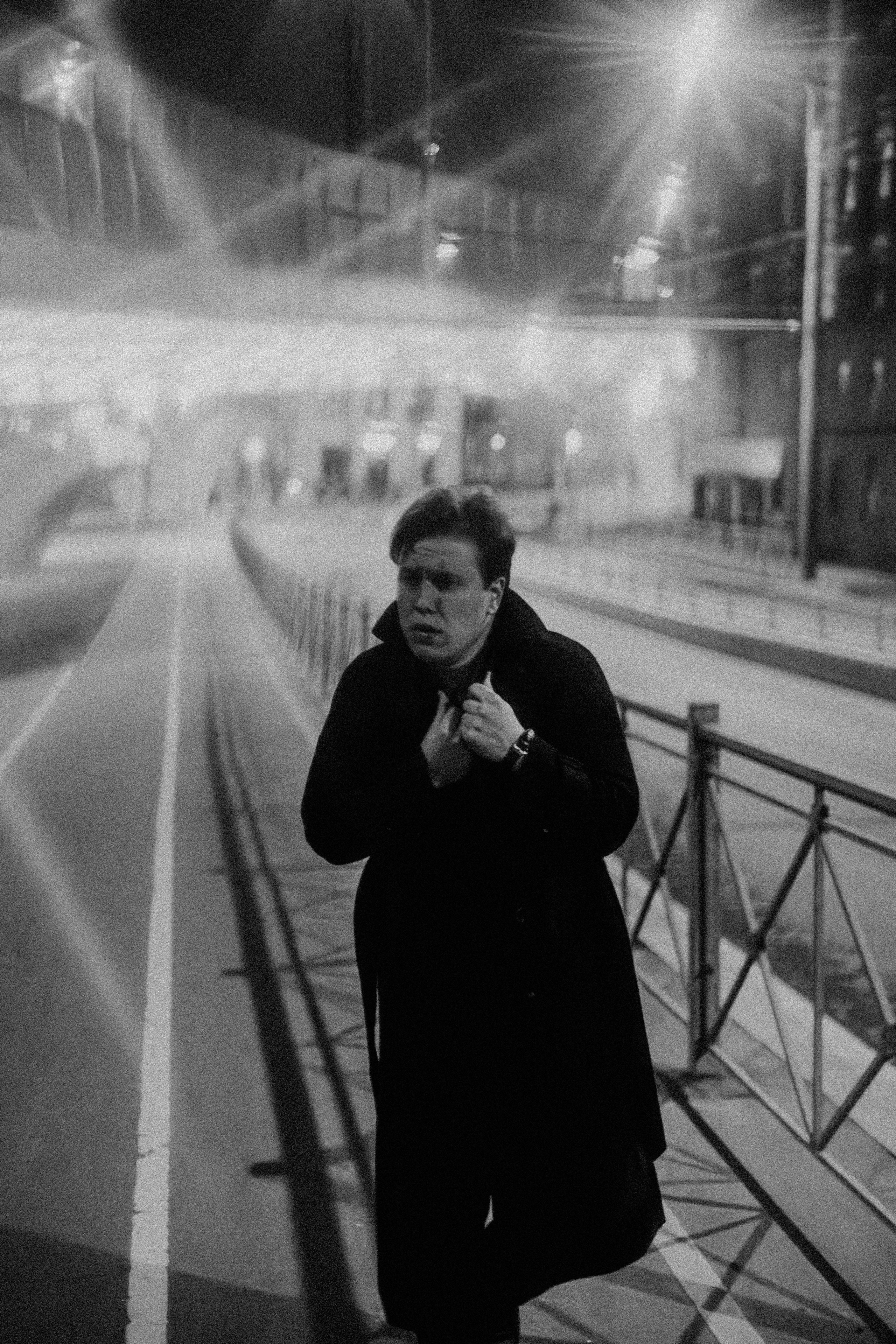 Молодой человек укутывается в плащ ночью