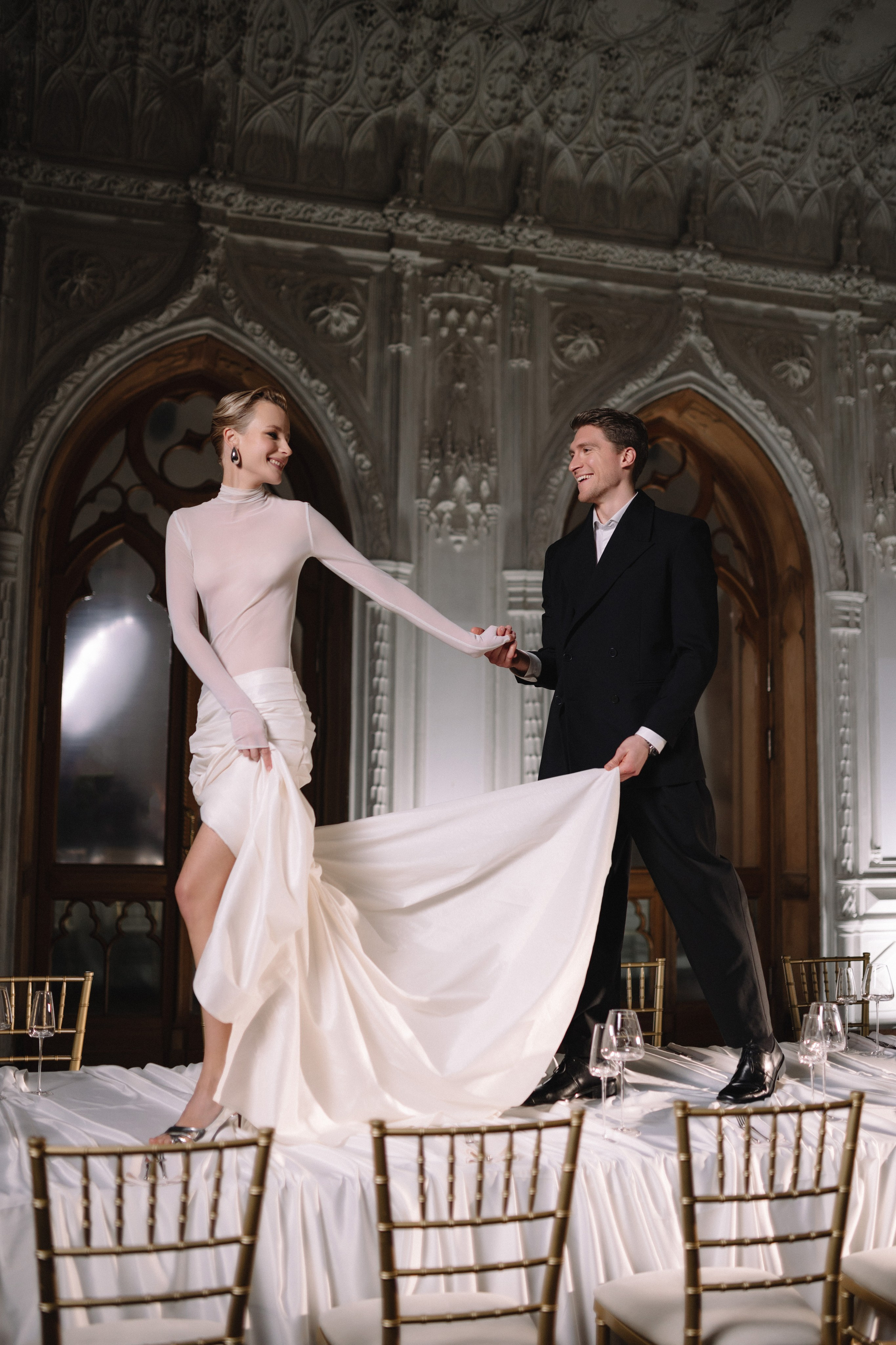 Жених бережно поправляет шелковый платок невесты, спускаясь по лестнице главного фойе.