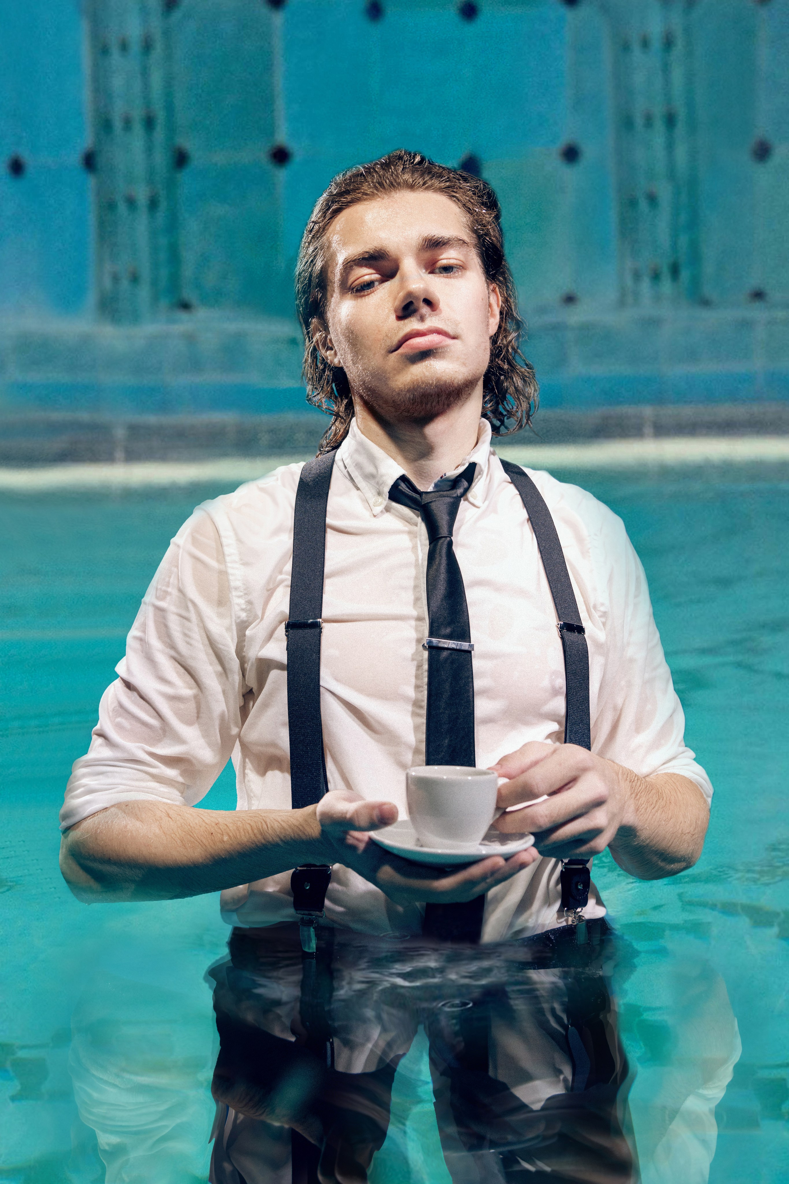 Художественное фото: мужчина по пояс стоит в бассейне с чашкой чая.