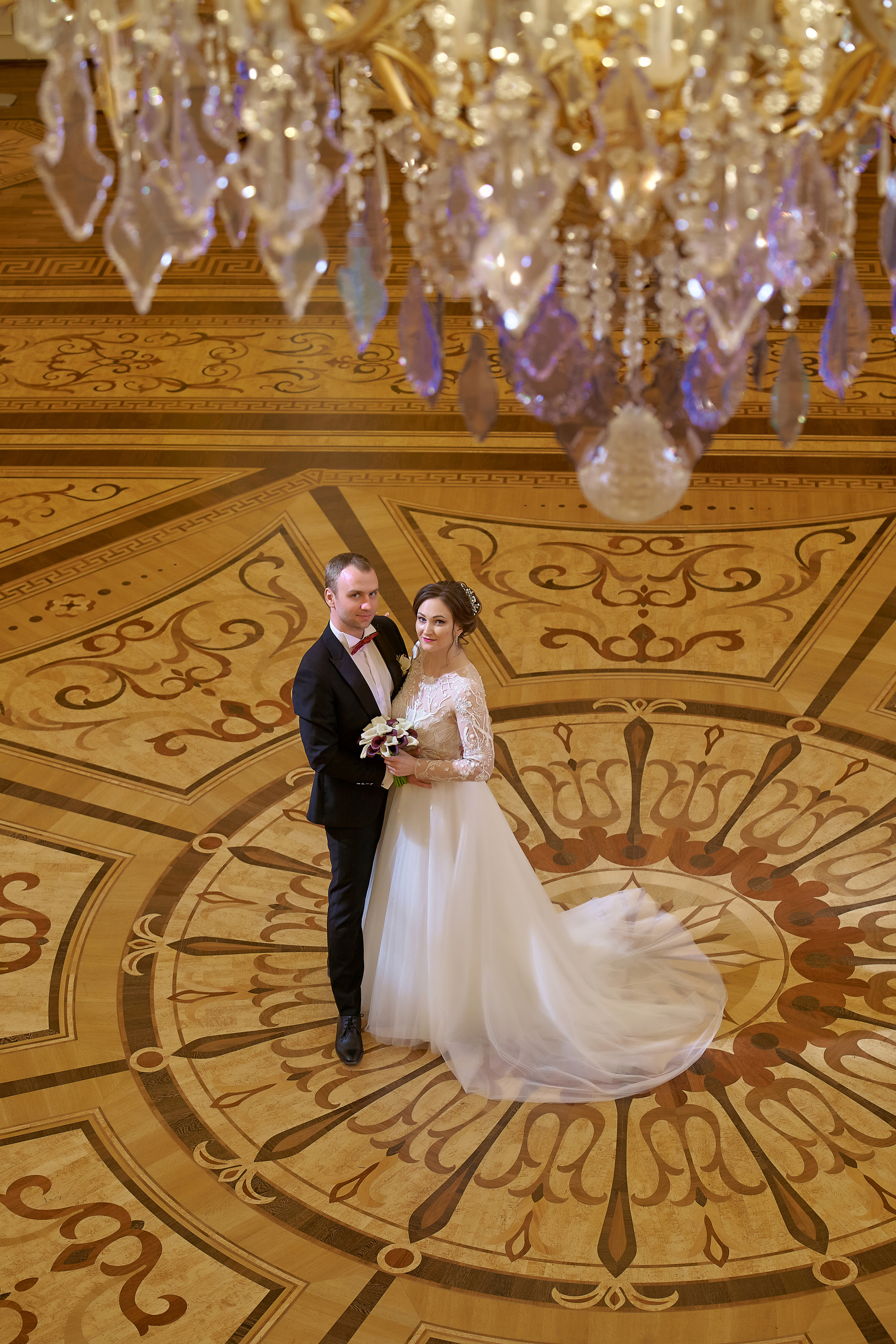 Молодожены позируют в красивом зале Царицино на фоне большой люстры Свадебная фотосъемка в Москве. Свадебный фотограф в Москве Сергей Гаварос. 