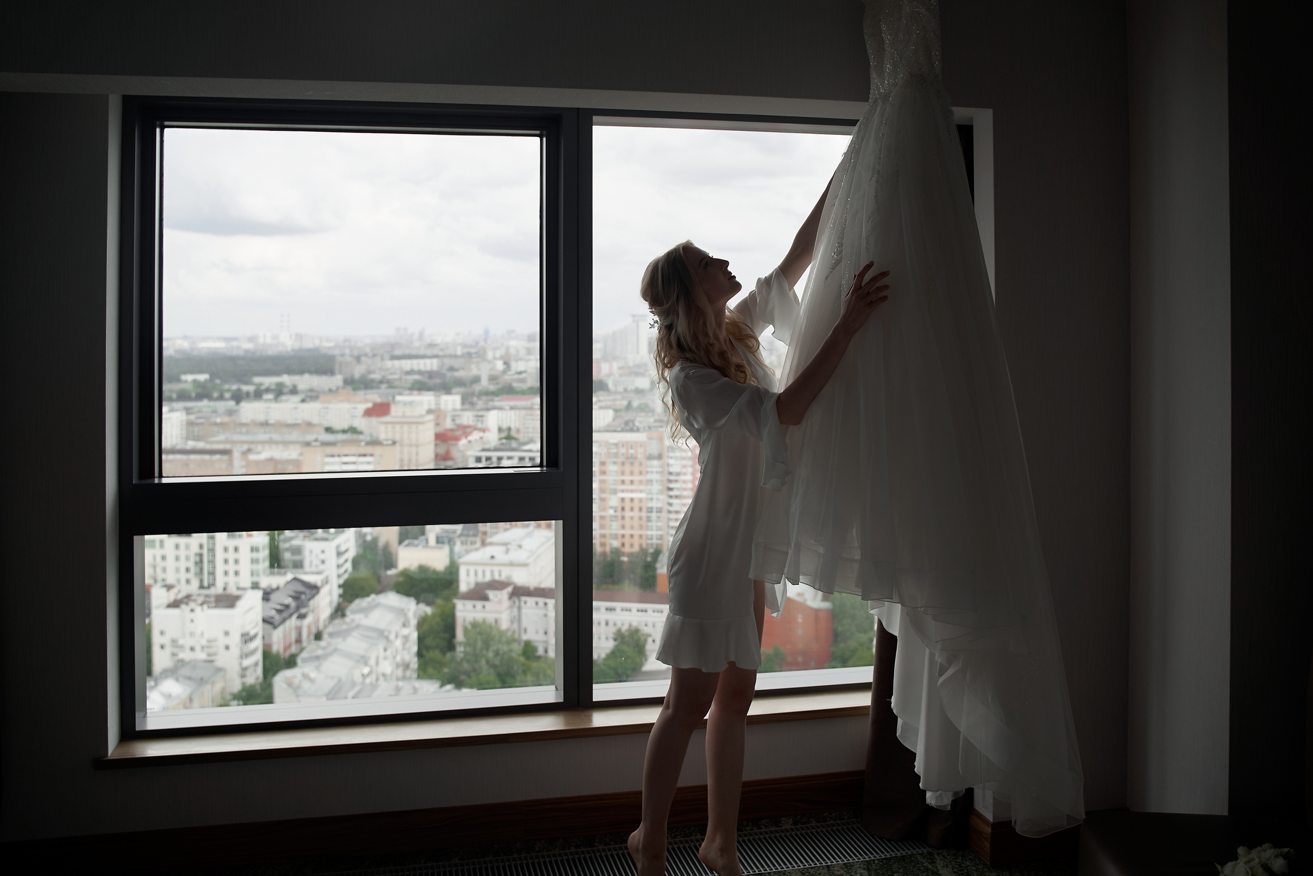 невеста со свадебным платьем у окна Свадебная фотосъемка в Москве. Свадебный фотограф в Москве  Сергей Гаварос.