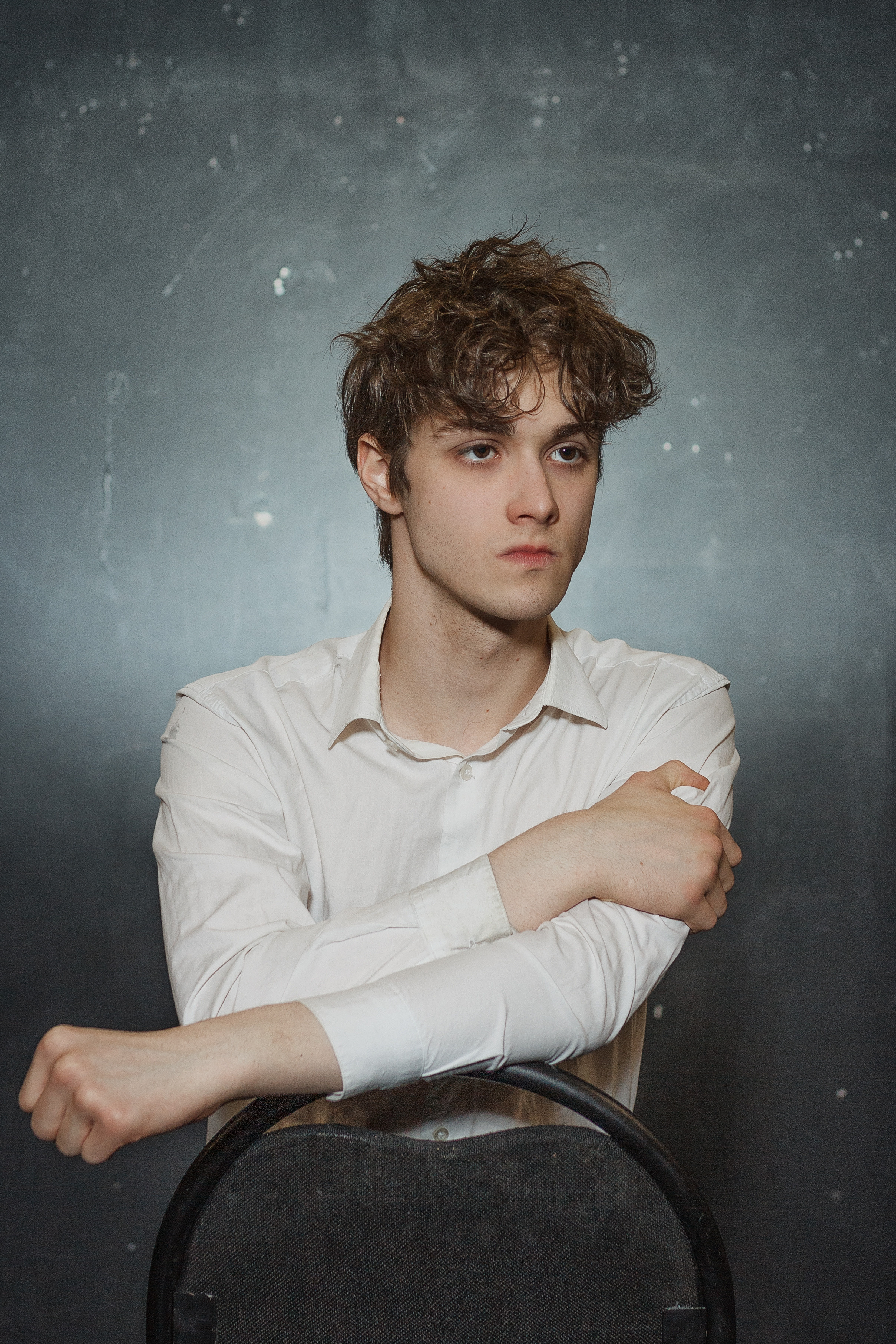 Парень в белой рубашке опирается на стул