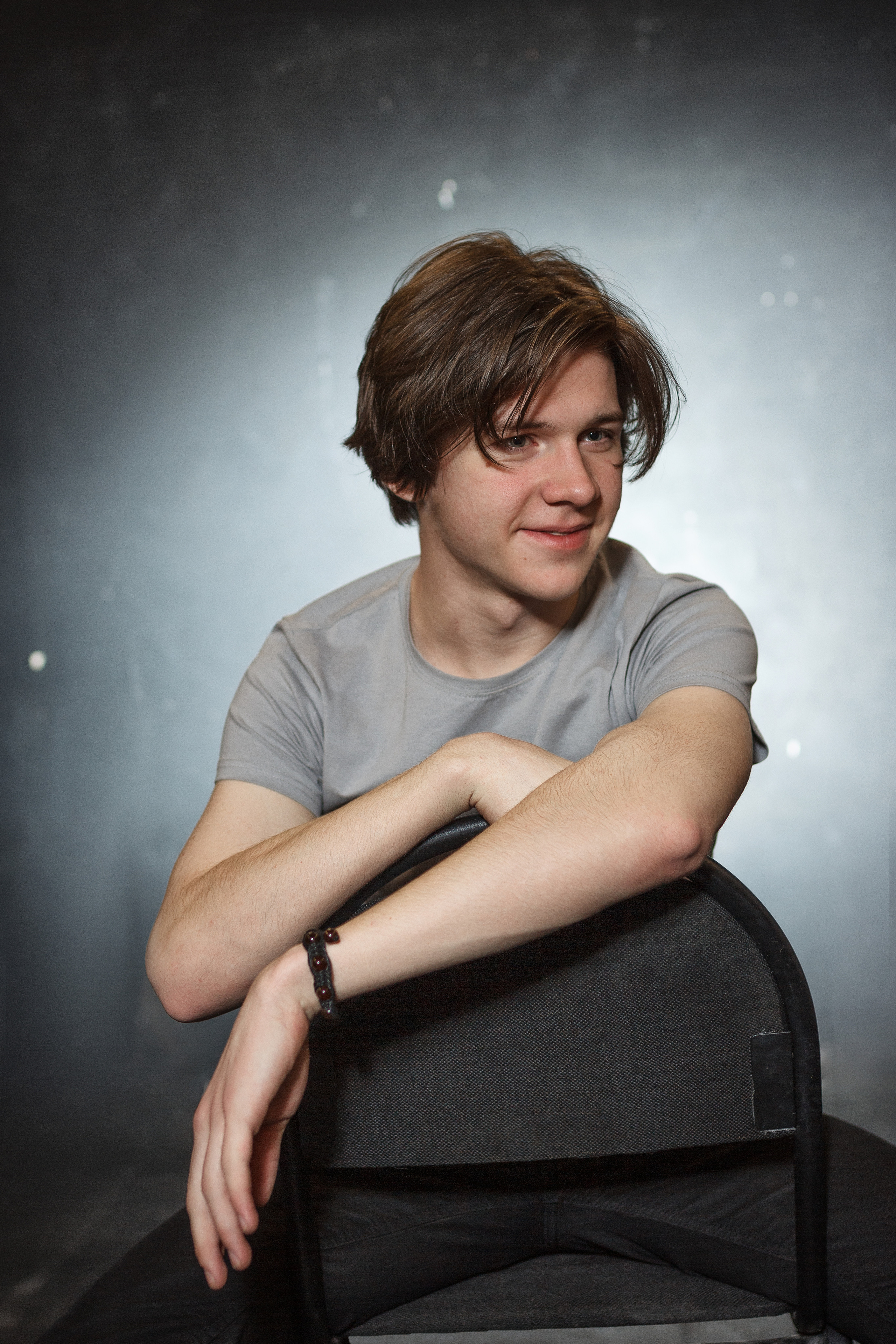 Молодой человек в футболке опирается на стул