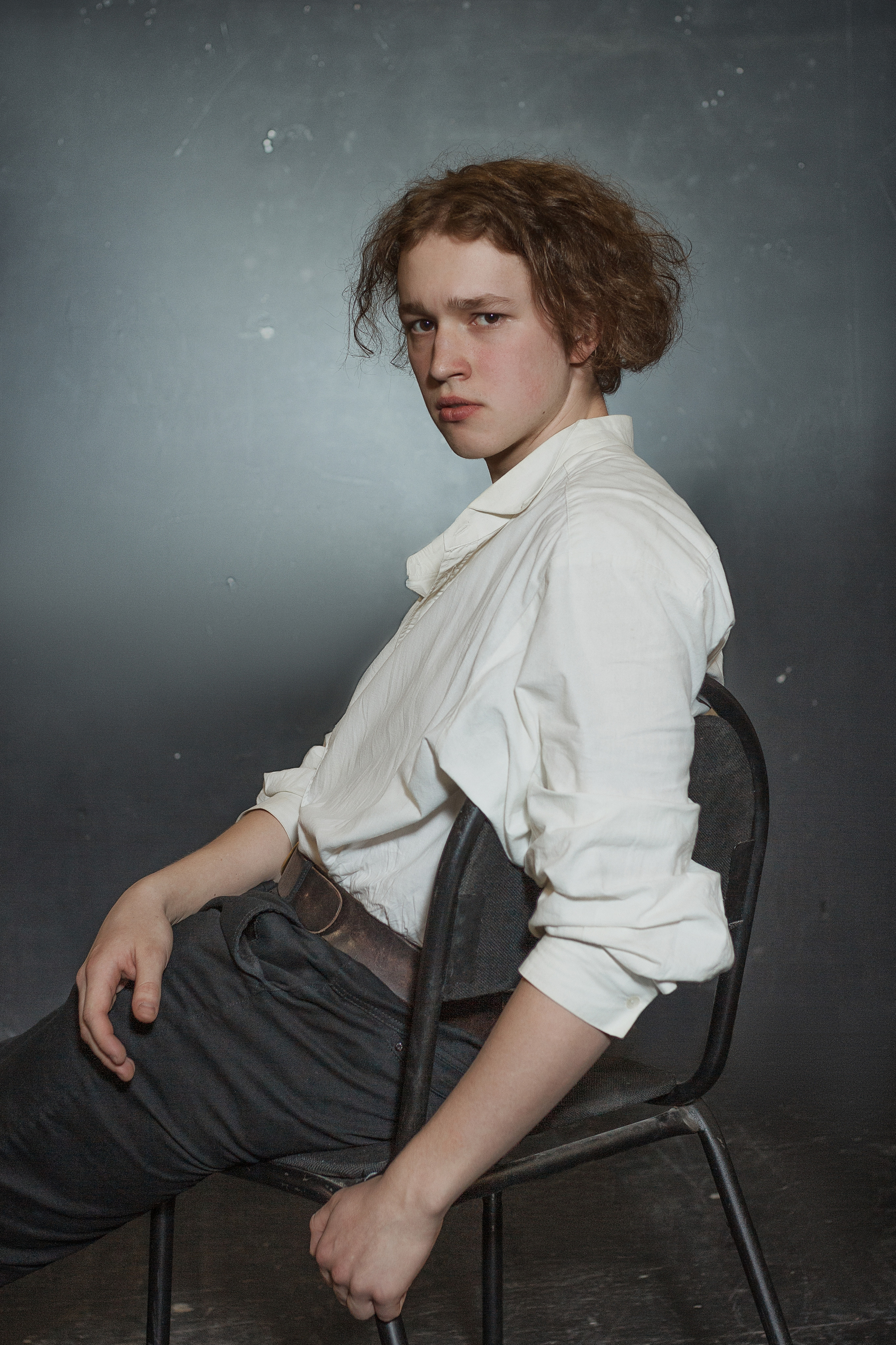 Юноша в свободной рубашке сидит на стуле