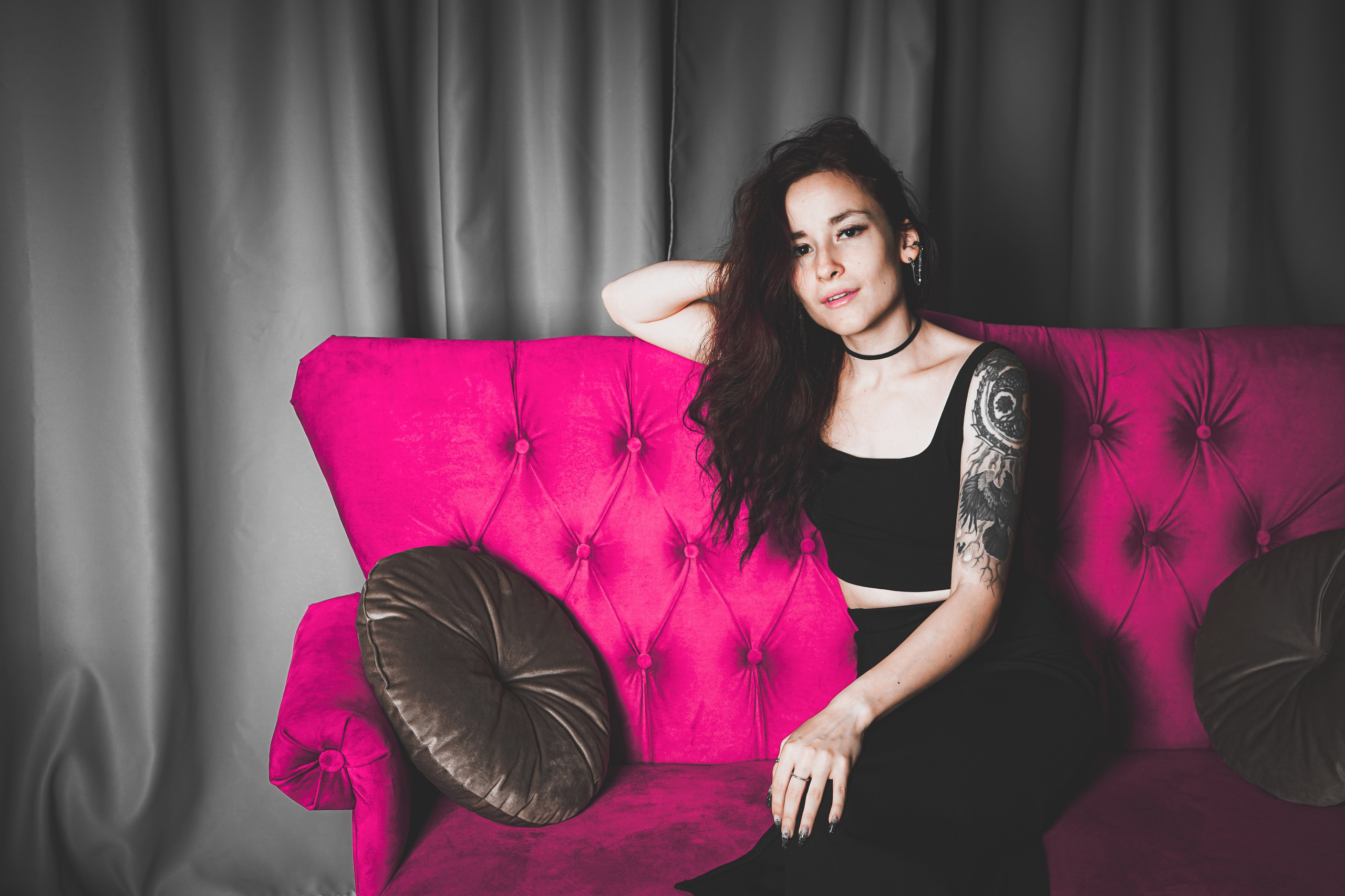 Красивая девушка с татуировкой сидит на ярко-розовом диване