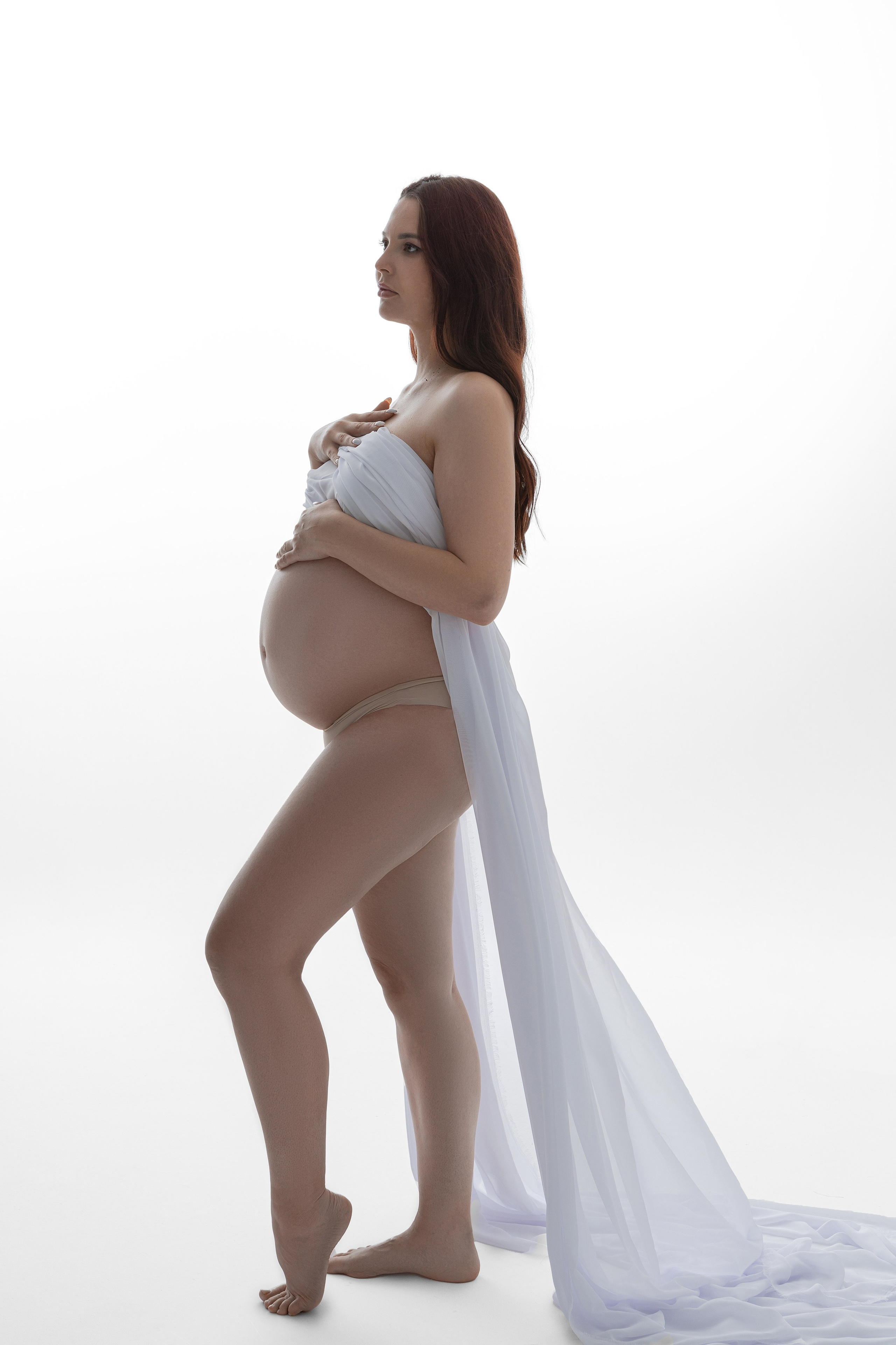 Беременная девушка на белом фоне держит в руках ткань