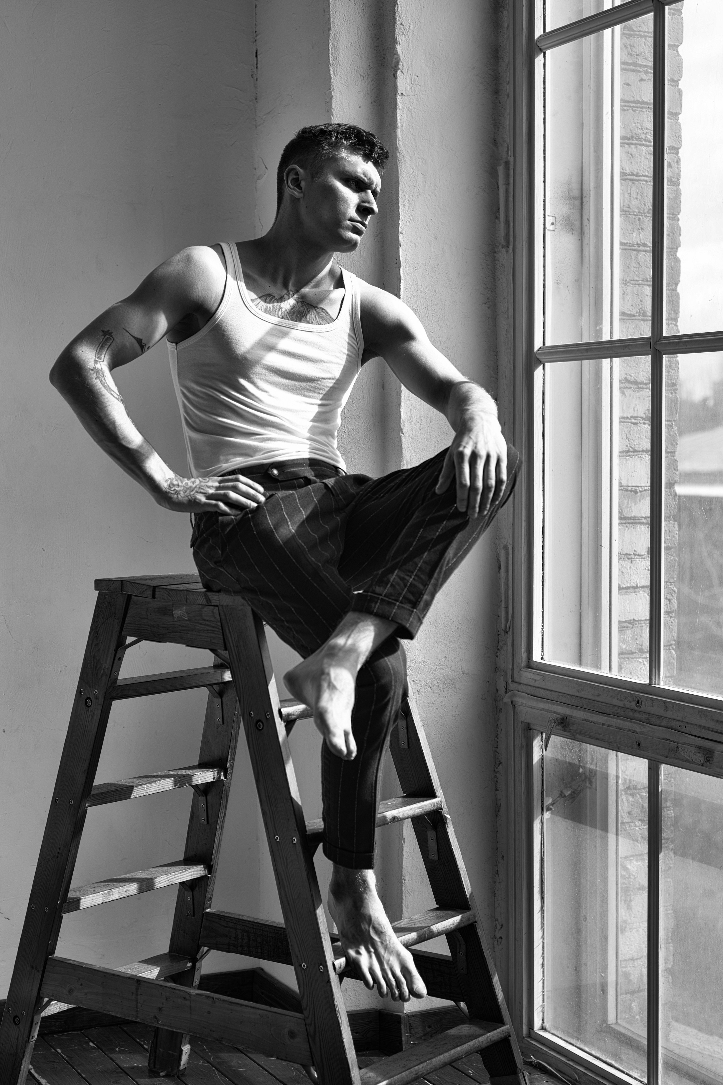 Мужчина на против окна сидит на стремянке в полосатых брюках 