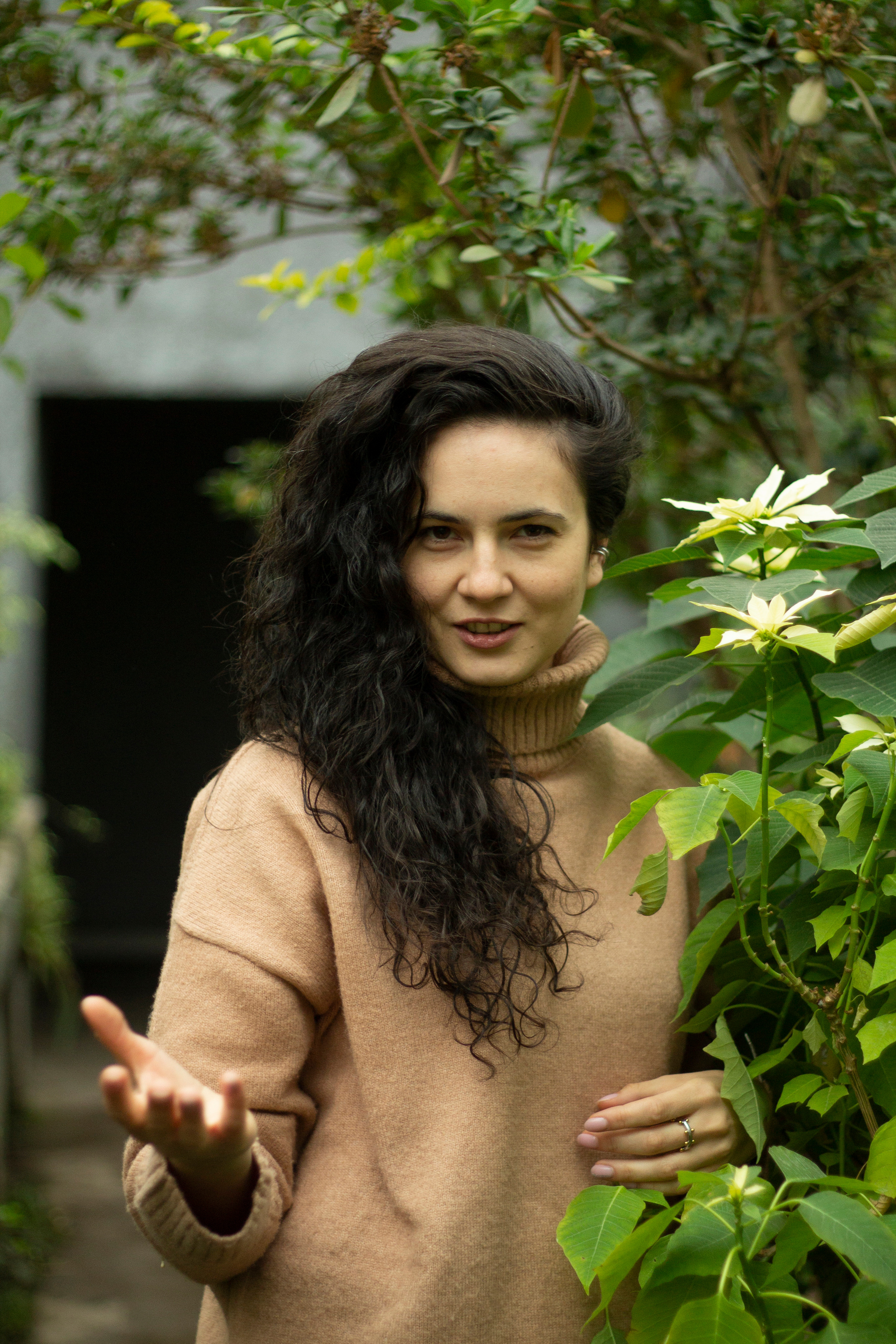 Таня Скрингер в бежевом свитере протягивает нам руку помощи на фоне цветов в оранжерее