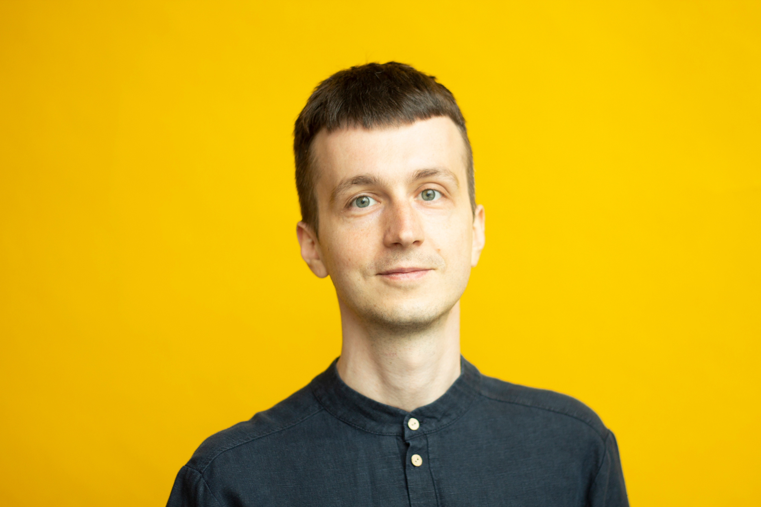 Парень в черной рубашке на желтом фоне смотрит в камеру  в Москве