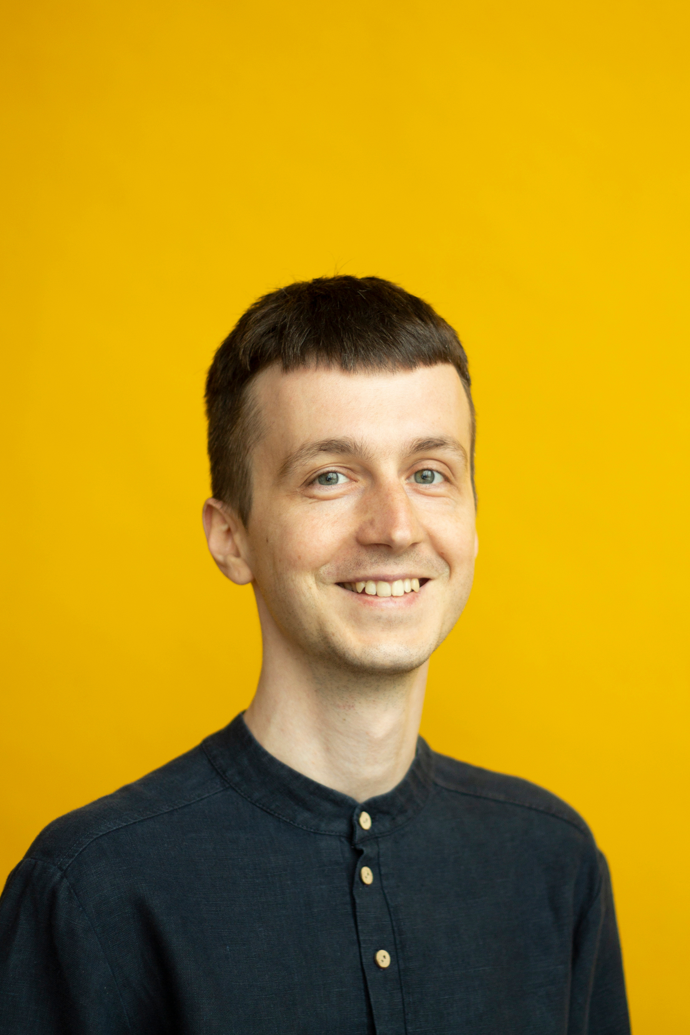 Мужчина в черном на желтом фоне смотрит в камеру и улыбается 