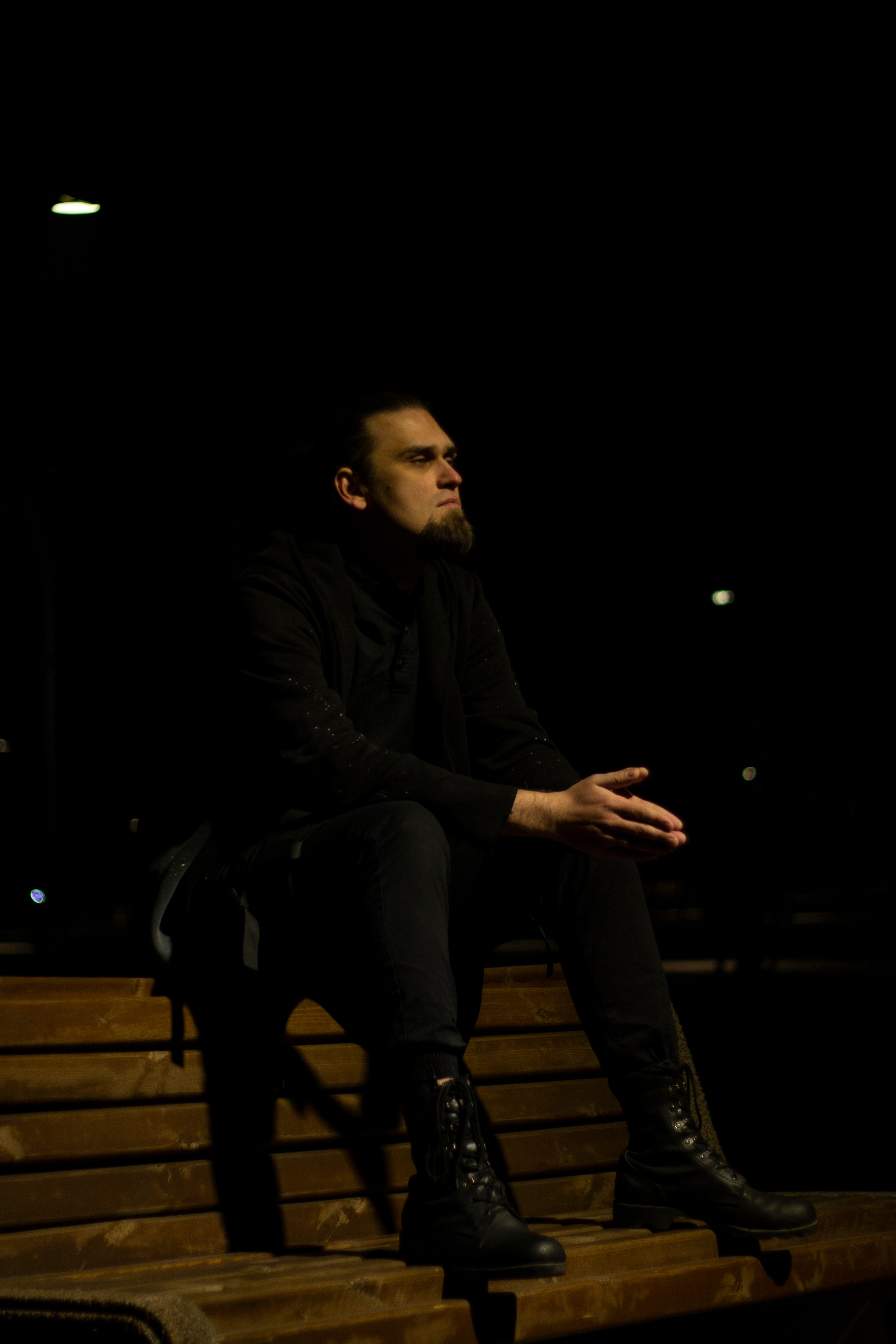 Мужчина в черной одежде сидит на скамейке в парке ночью