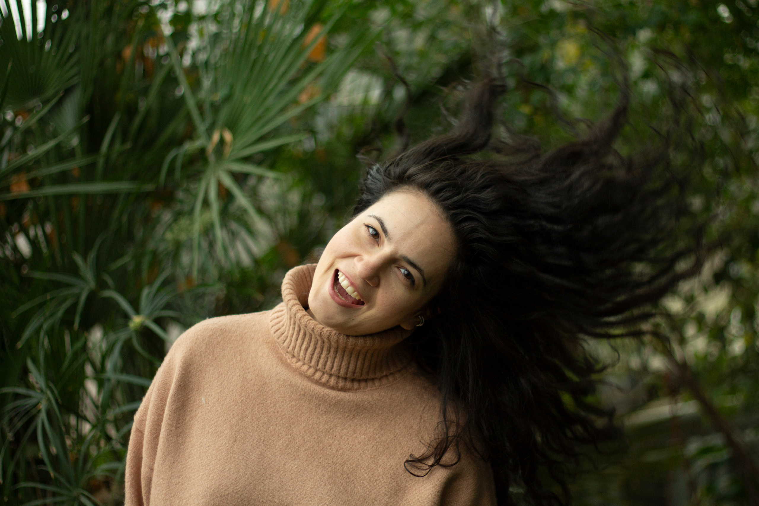 Девушка с длинными кудрявыми волосами машет головой в оранжерее