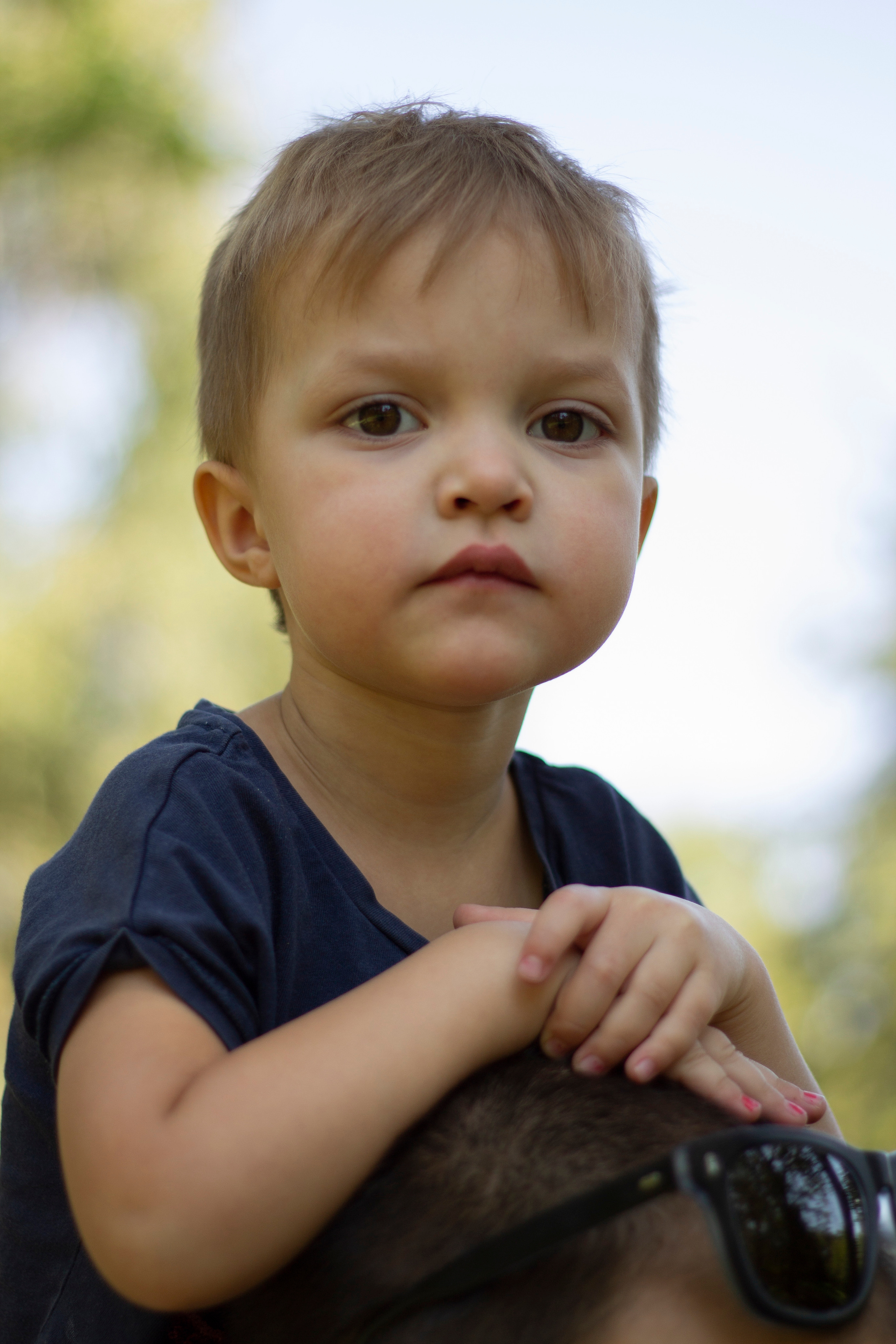 Девочка сидит на плечах у отца и смотрит в камеру