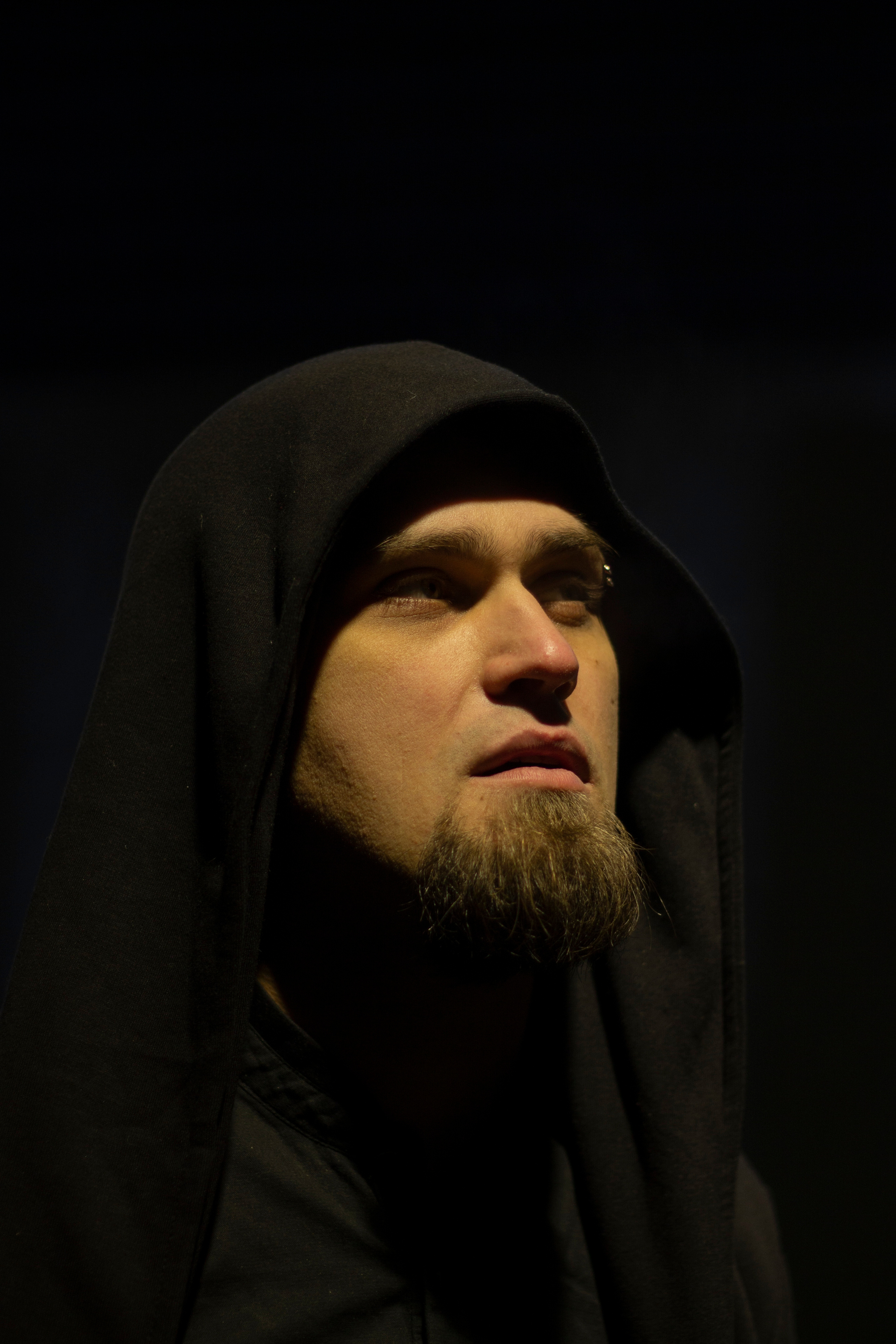 Портрет мужчины с бородой в черном капюшоне в свете фонаря ночного города