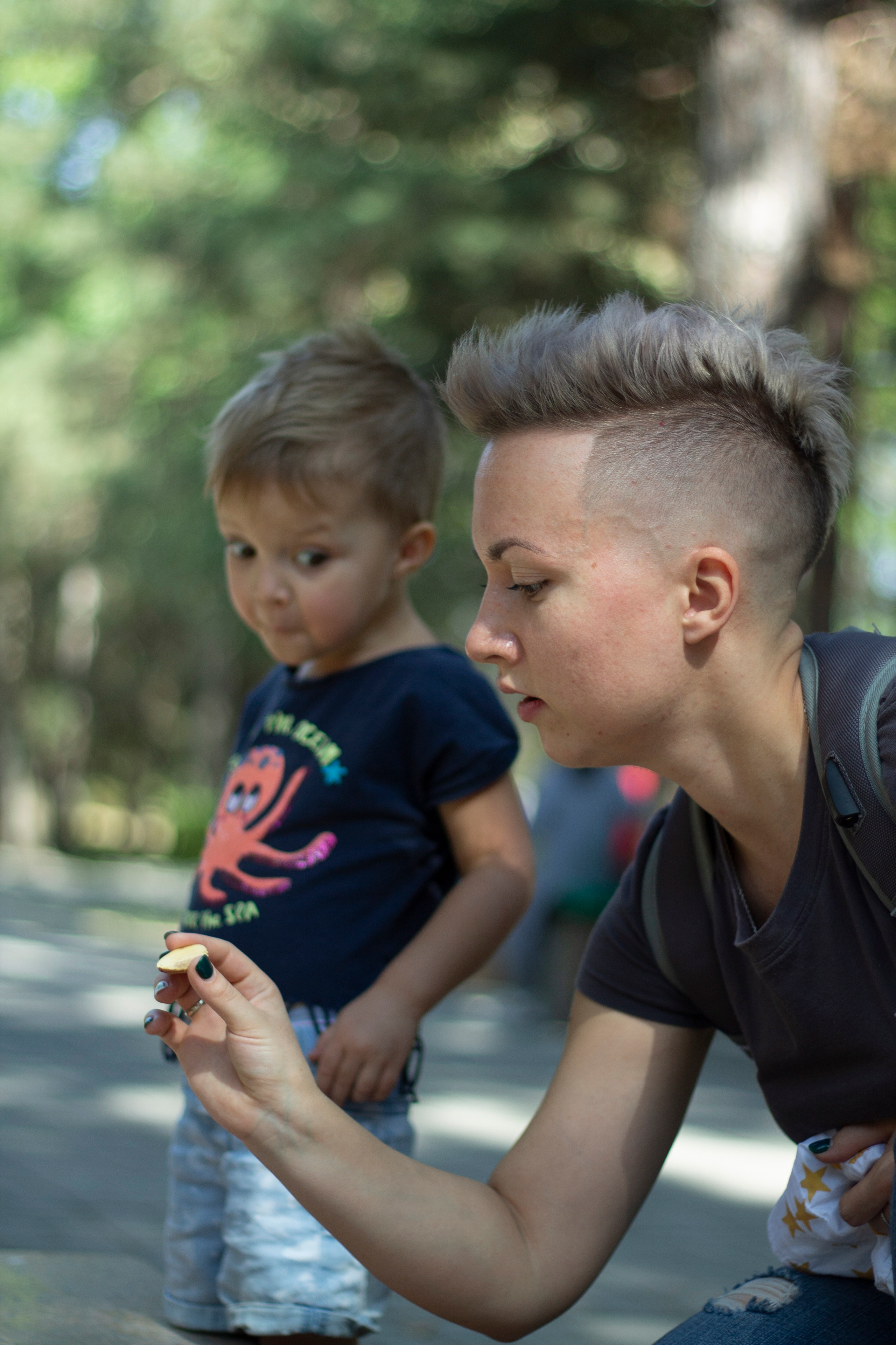 Мама с короткой стрижкой показывает что-то дочери на заднем плане