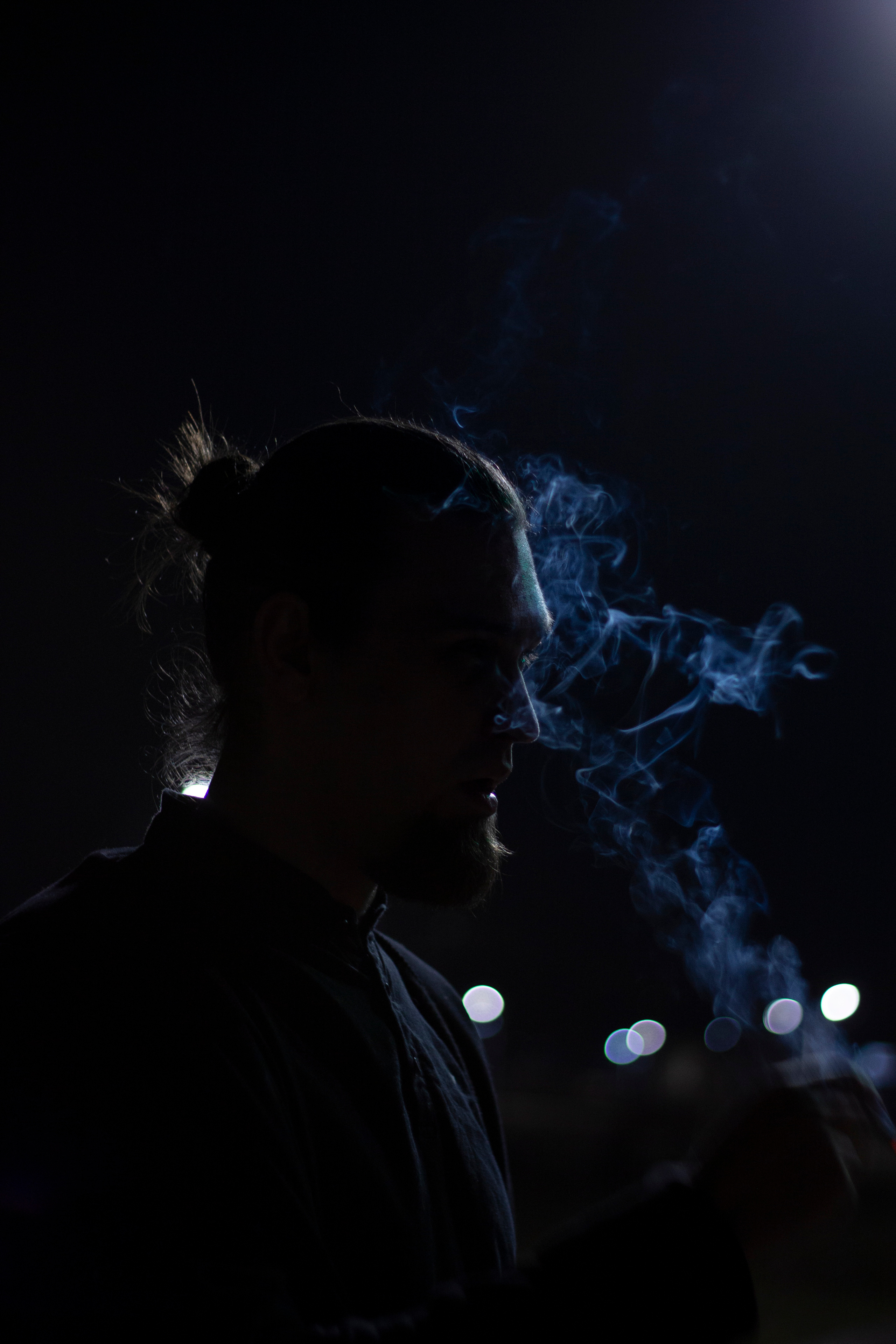 Дым сигареты мужчины с бородой подсвечиваестя огнями города