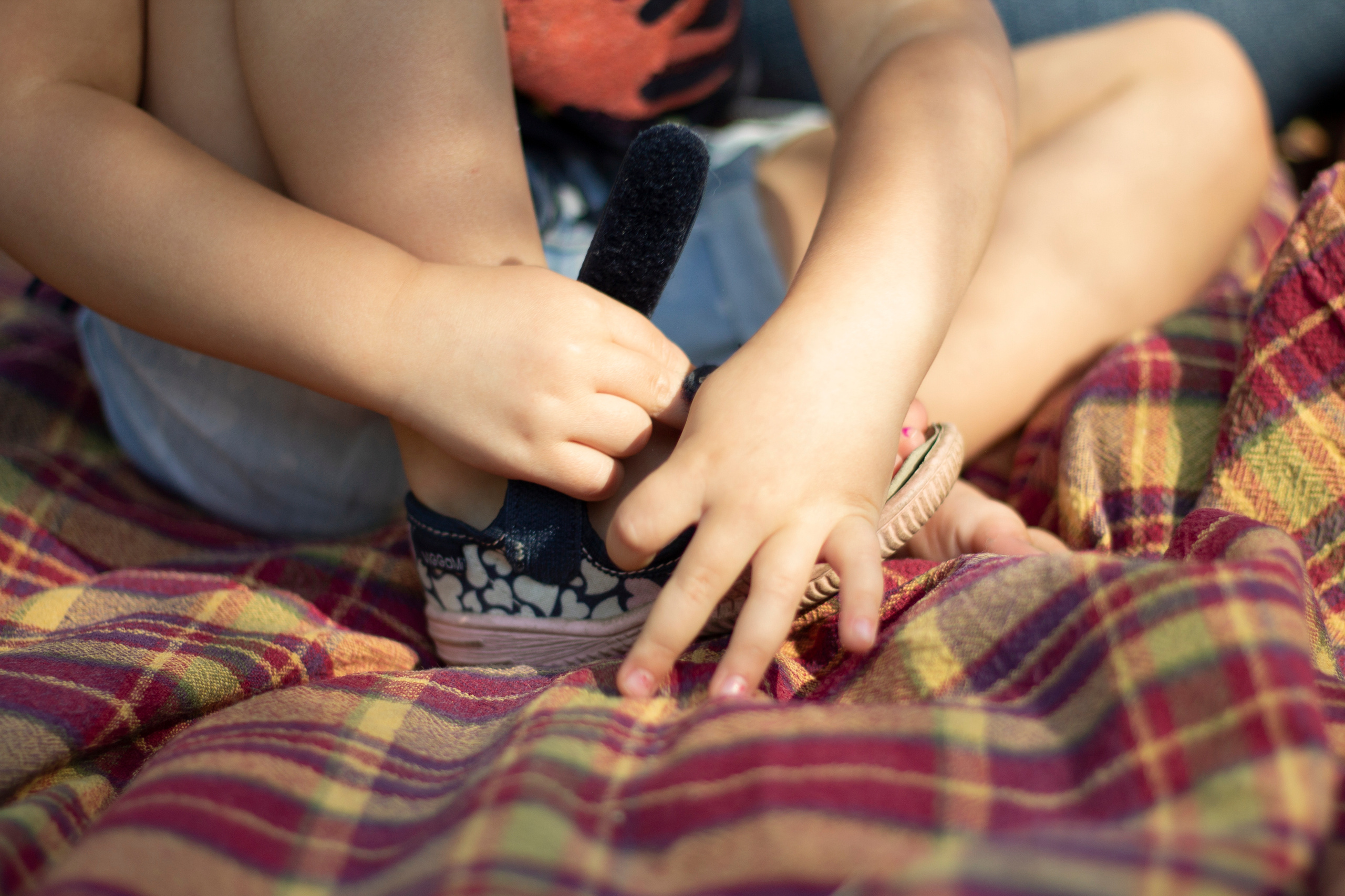 Маленькая девочка на клетчатом пледе застегивает обувь самостоятельно