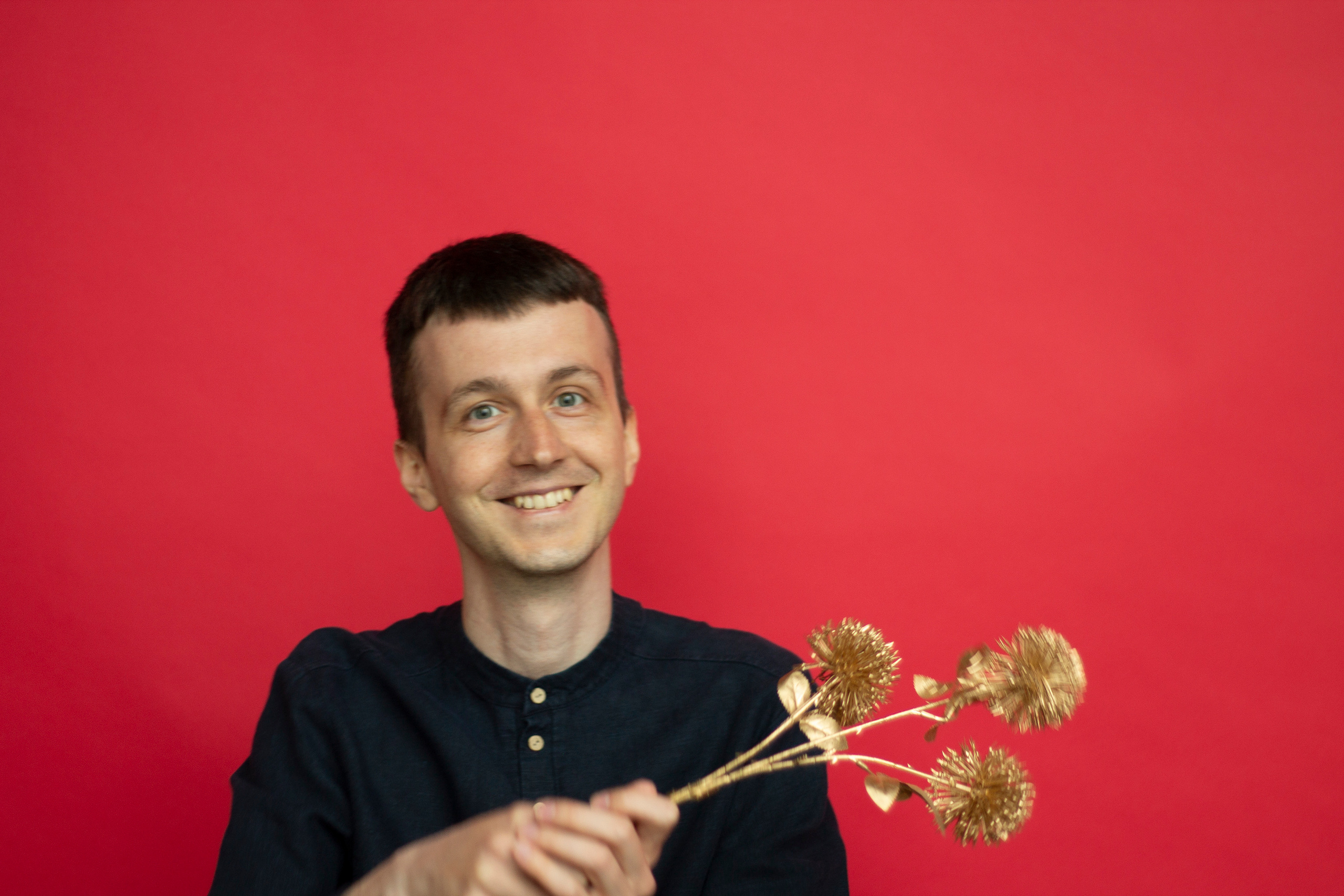 Мужчина в черной рубашке на красном фоне держит в руках золотую колючку город Москва