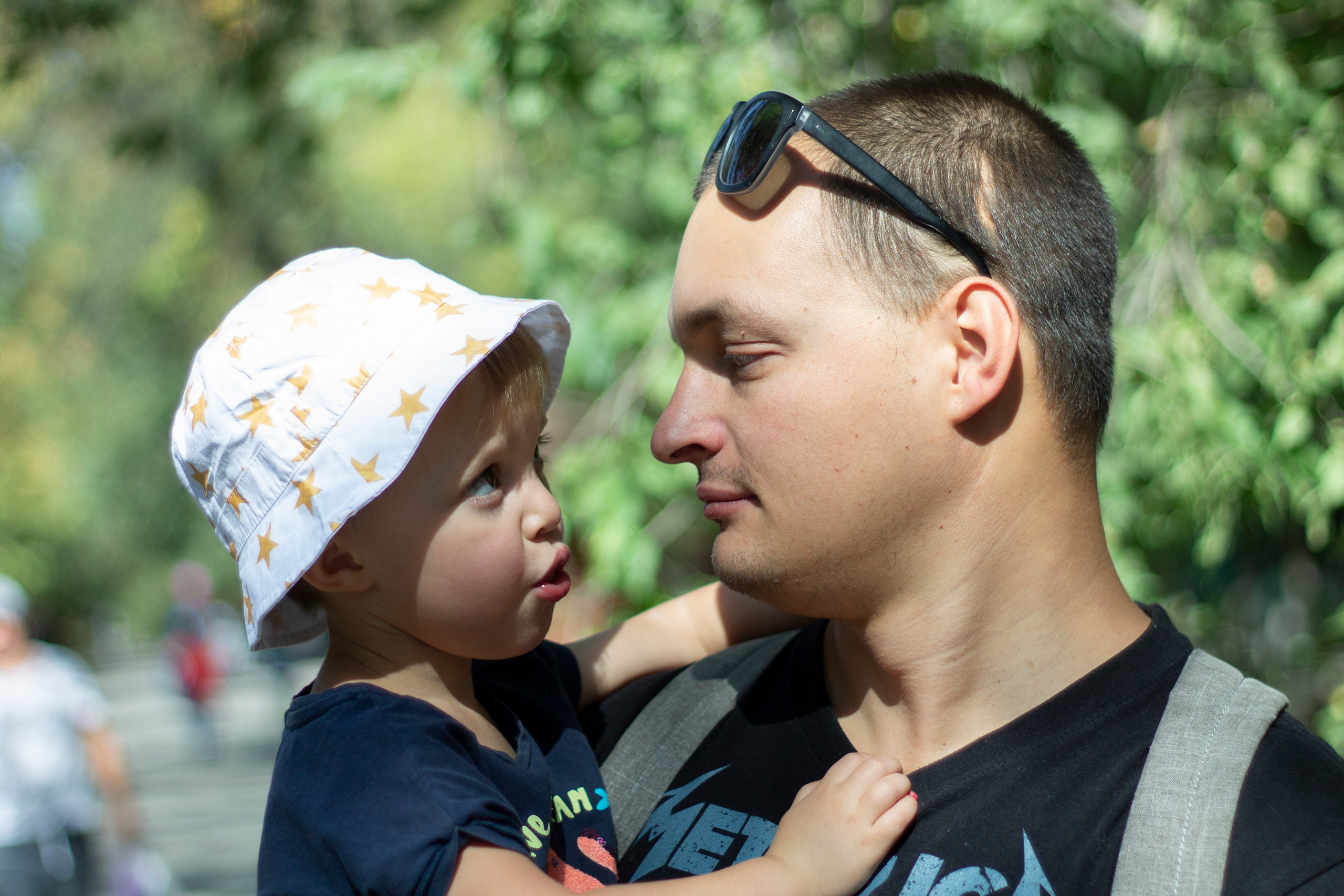 Папа в солнцезащитных очках на лбу держит дочь в светлой панаме на руках они смотрят друг на друга