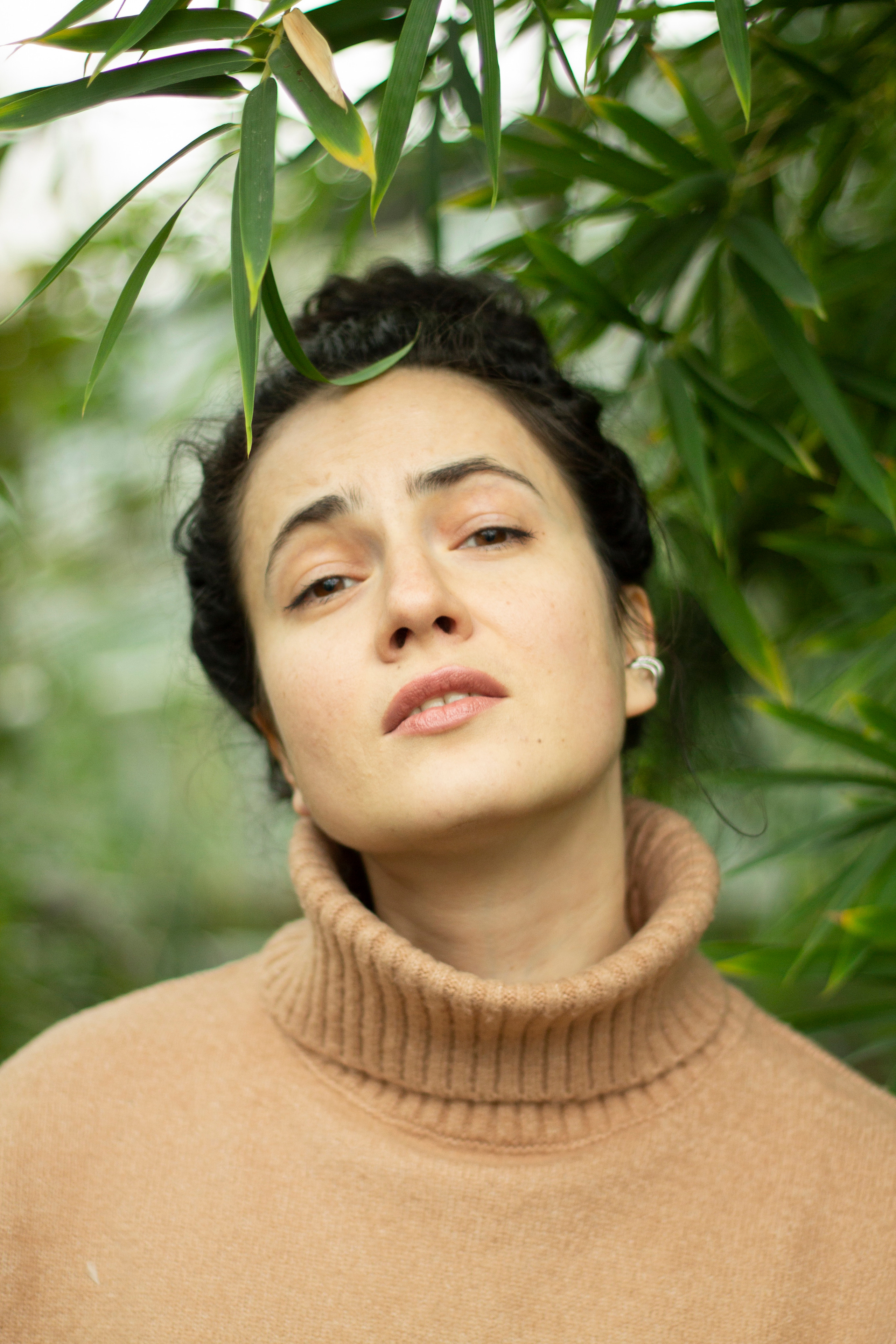 Девушка в бежевом свитере с дулькой на голове пафосно смотрит в камеру