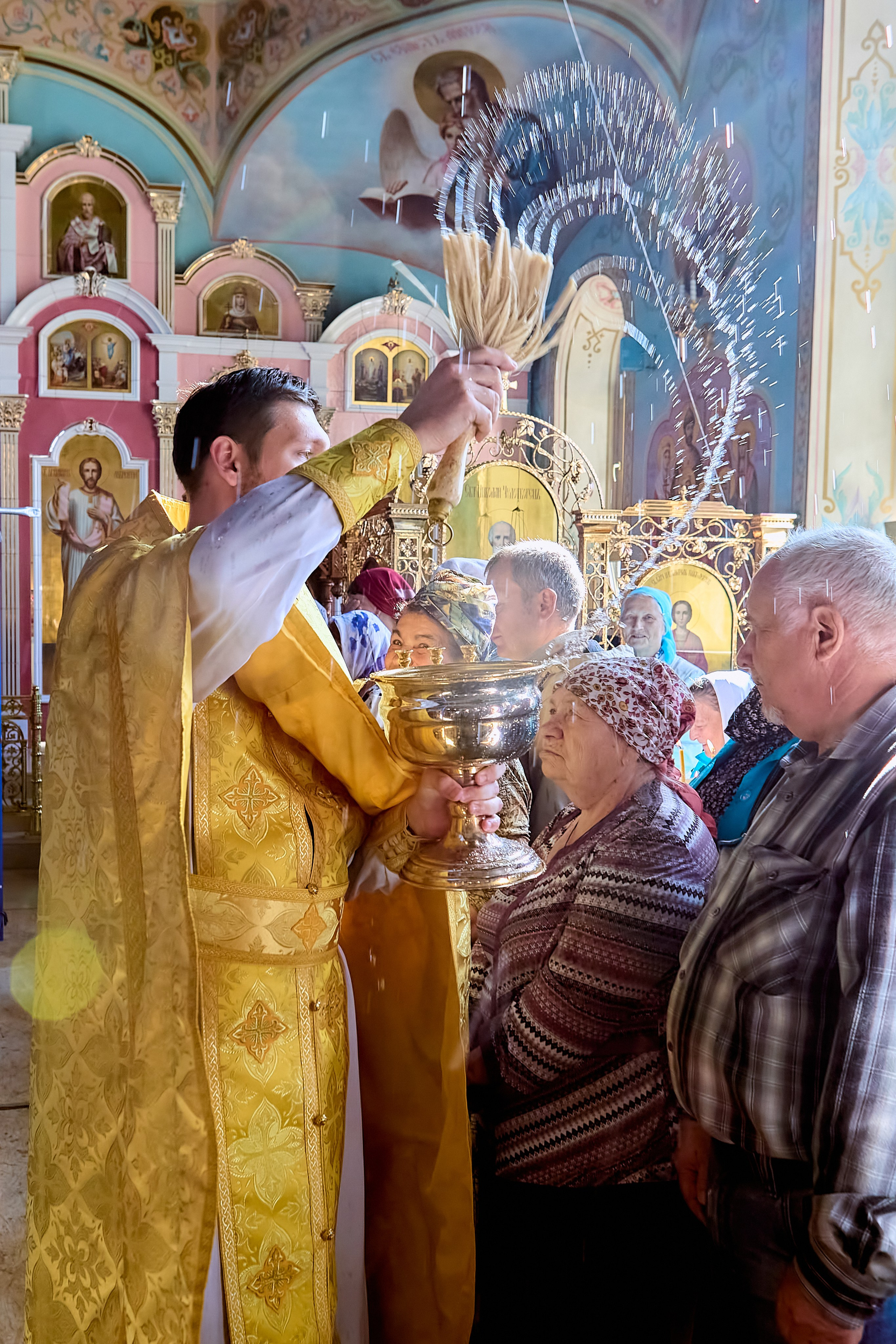 Священник окропляет прихожан святой водой и  капельки воды застыли в воздухе