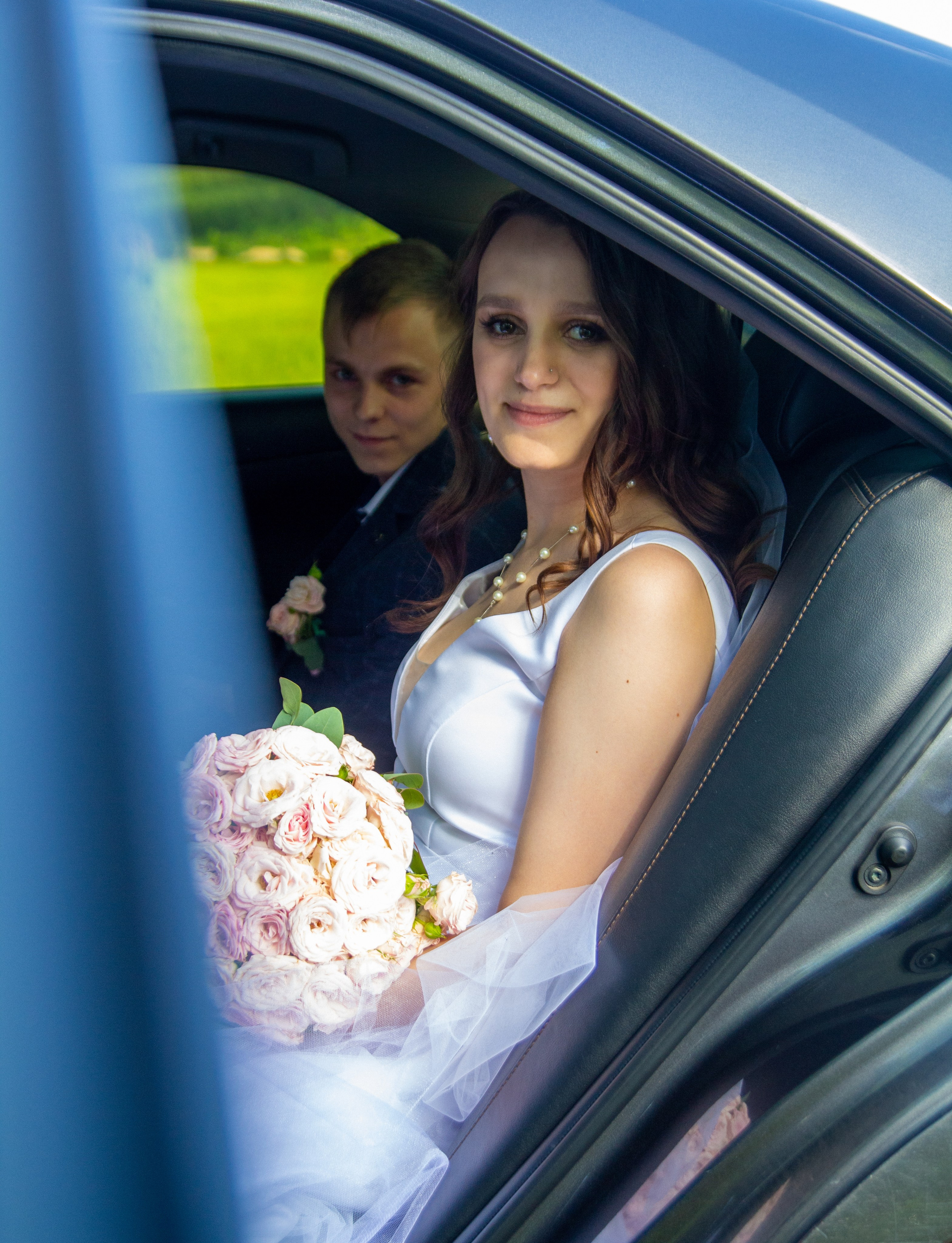 Невеста в машине с букетом и жених на заднем плане — момент перед или после церемонии.