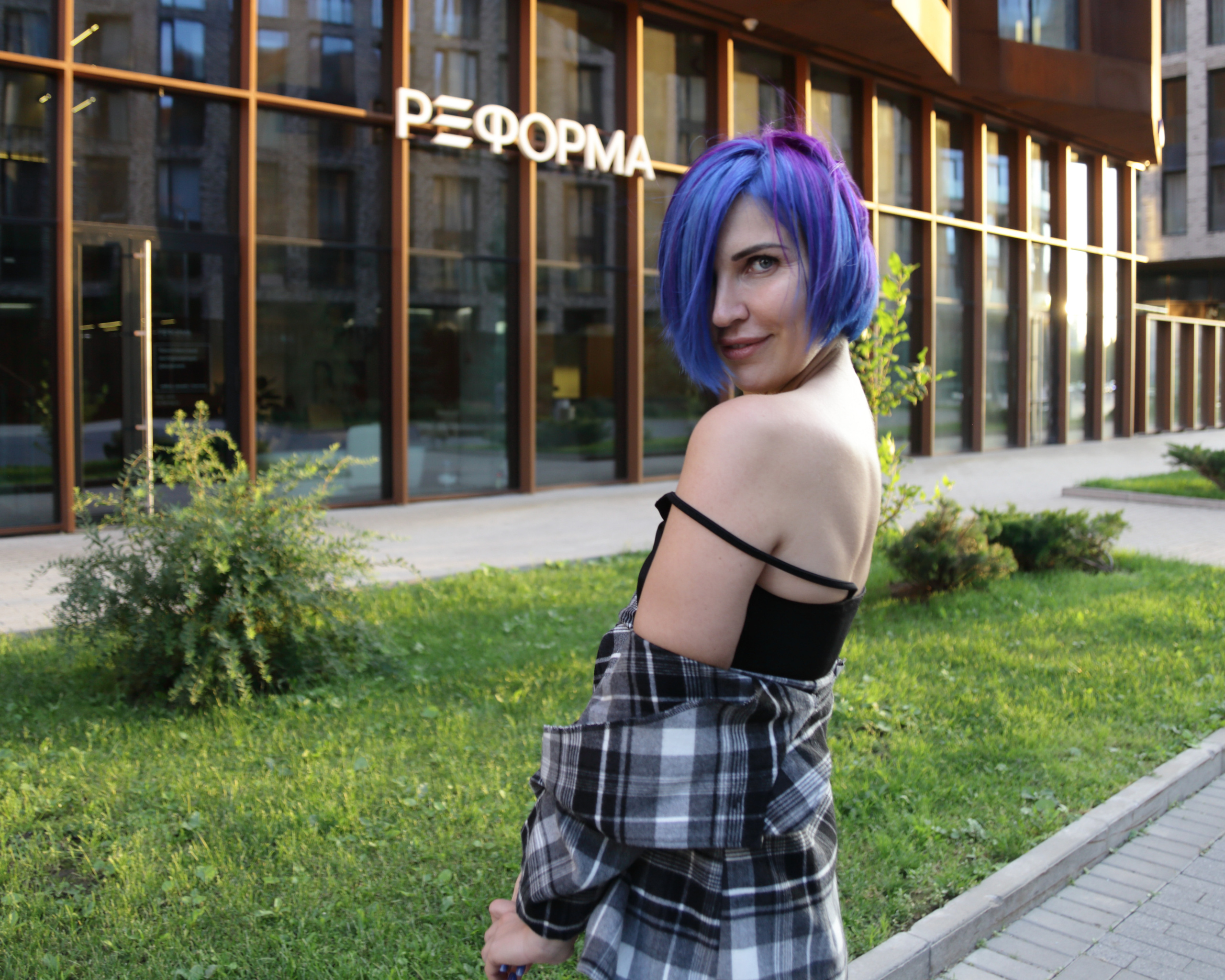 Девушка с синими волосами позирует на фоне городской архитектуры