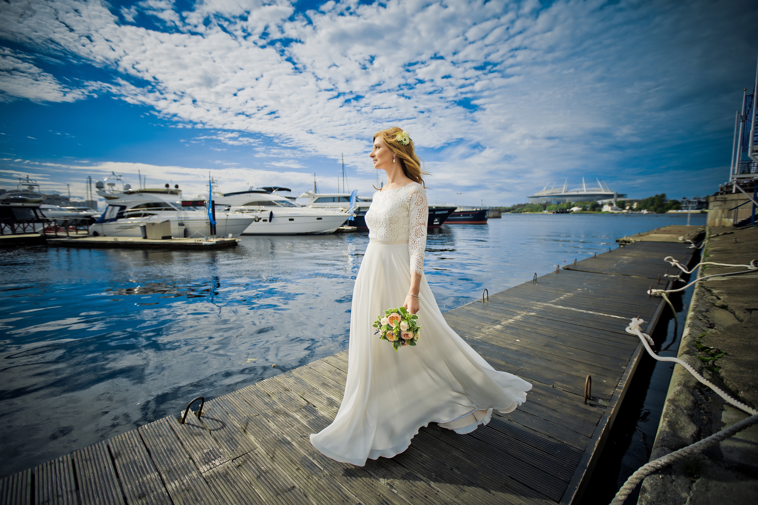 невеста идет по причалу на фоне яхт неба и стадиона