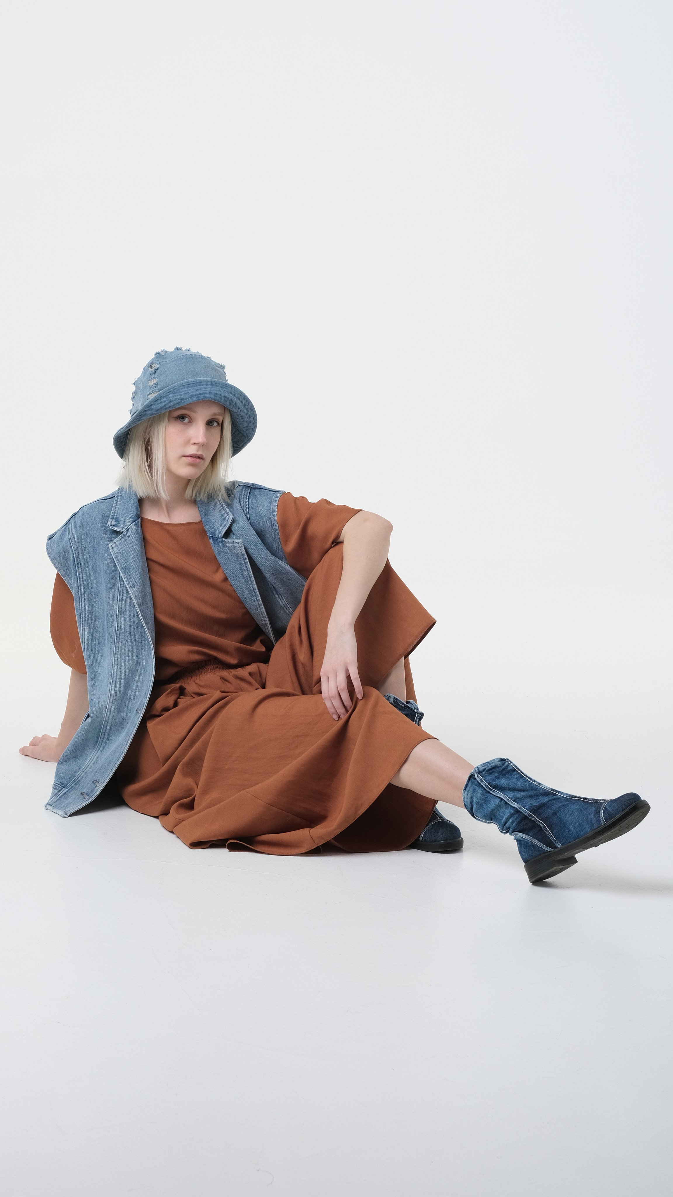 Фото сидя на циклораме для МП - Ozon, WB, LaModa. Девушка позирует сидя на циклораме в светло-коричневом костюме, в джинсовой жилетке и джинсовой панаме.