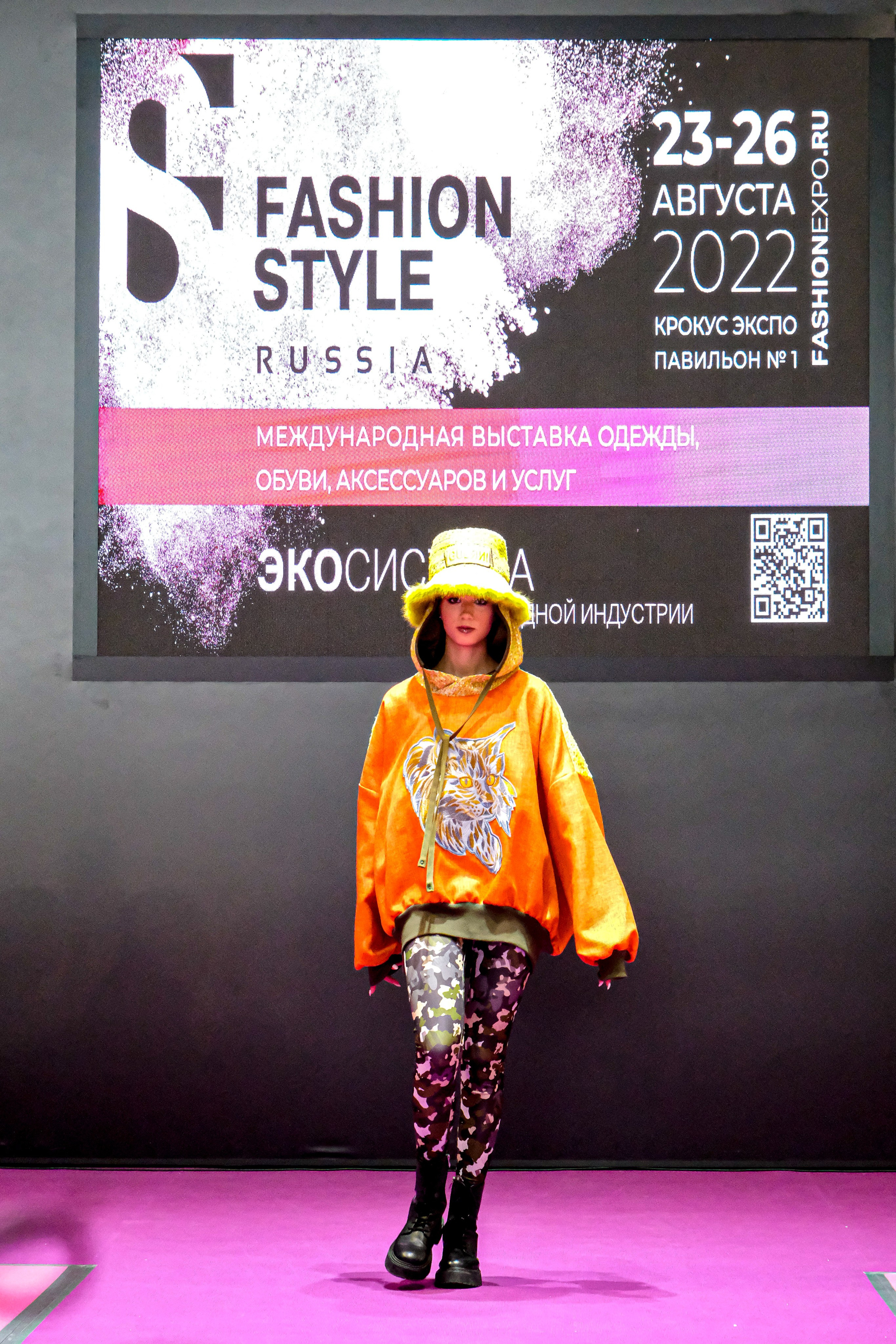  "Модели в ярких нарядах проходят по подиуму во время показа мод, освещенные яркими софитами и окруженные восторженными зрителями."