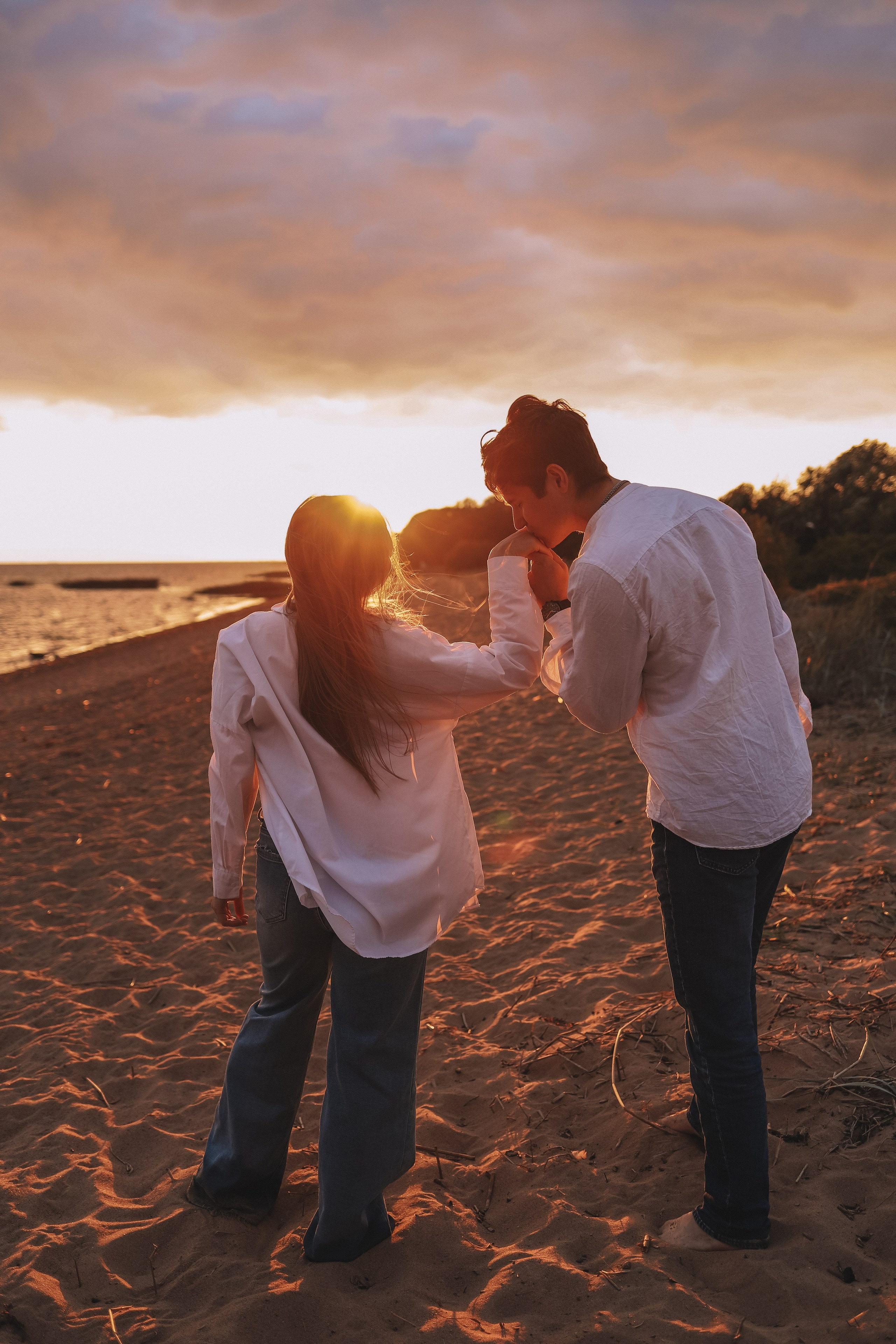 Пара держится за руки и идёт по пляжу на закате