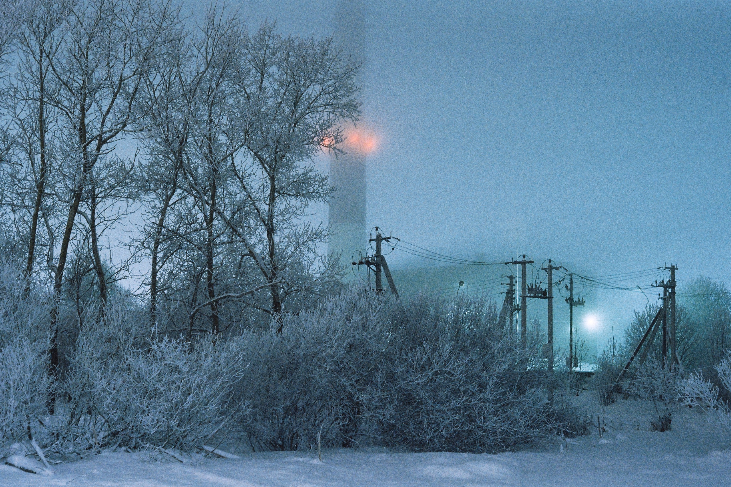 Морозный ночной пейзаж, ночной вид на котельную станцию в огнях на фоне заиндевевших деревьев. Санкт-Петербург, Россия