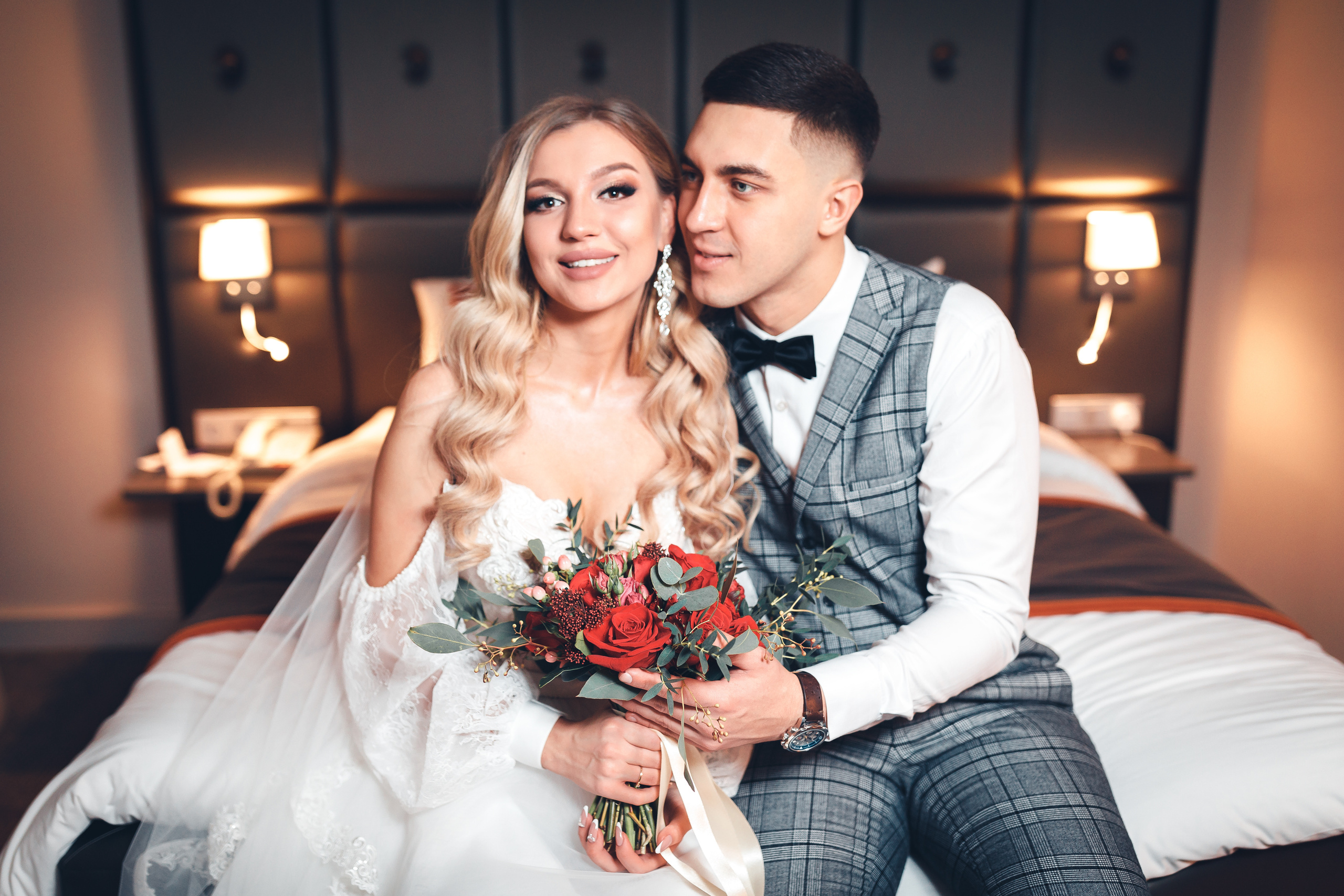 Жених и невеста красиво позируют на кровати на свадьбе в номере отедя