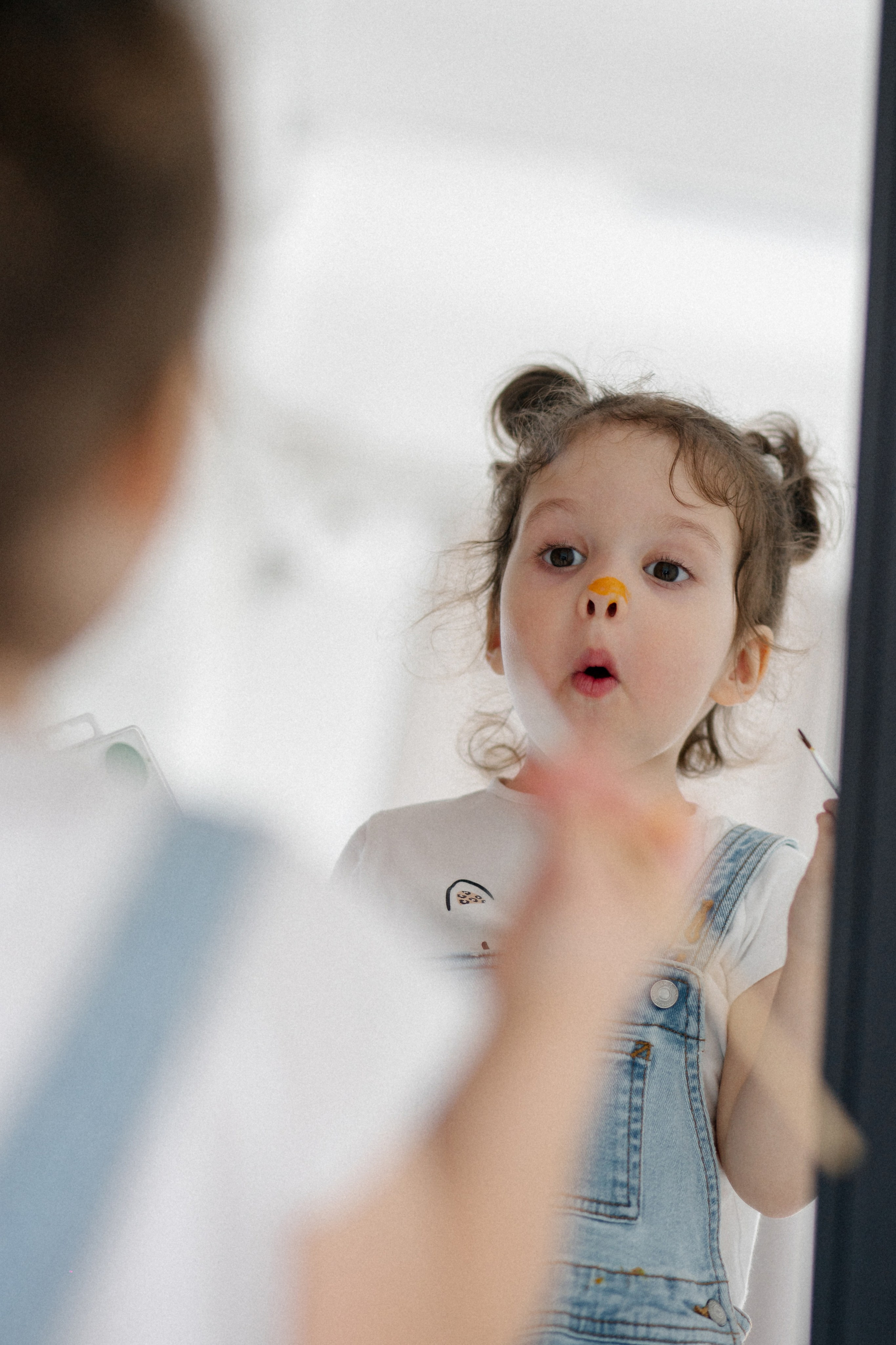 девочка перед зеркалом восторженно смотрит на свое разрисованное красками отражение 