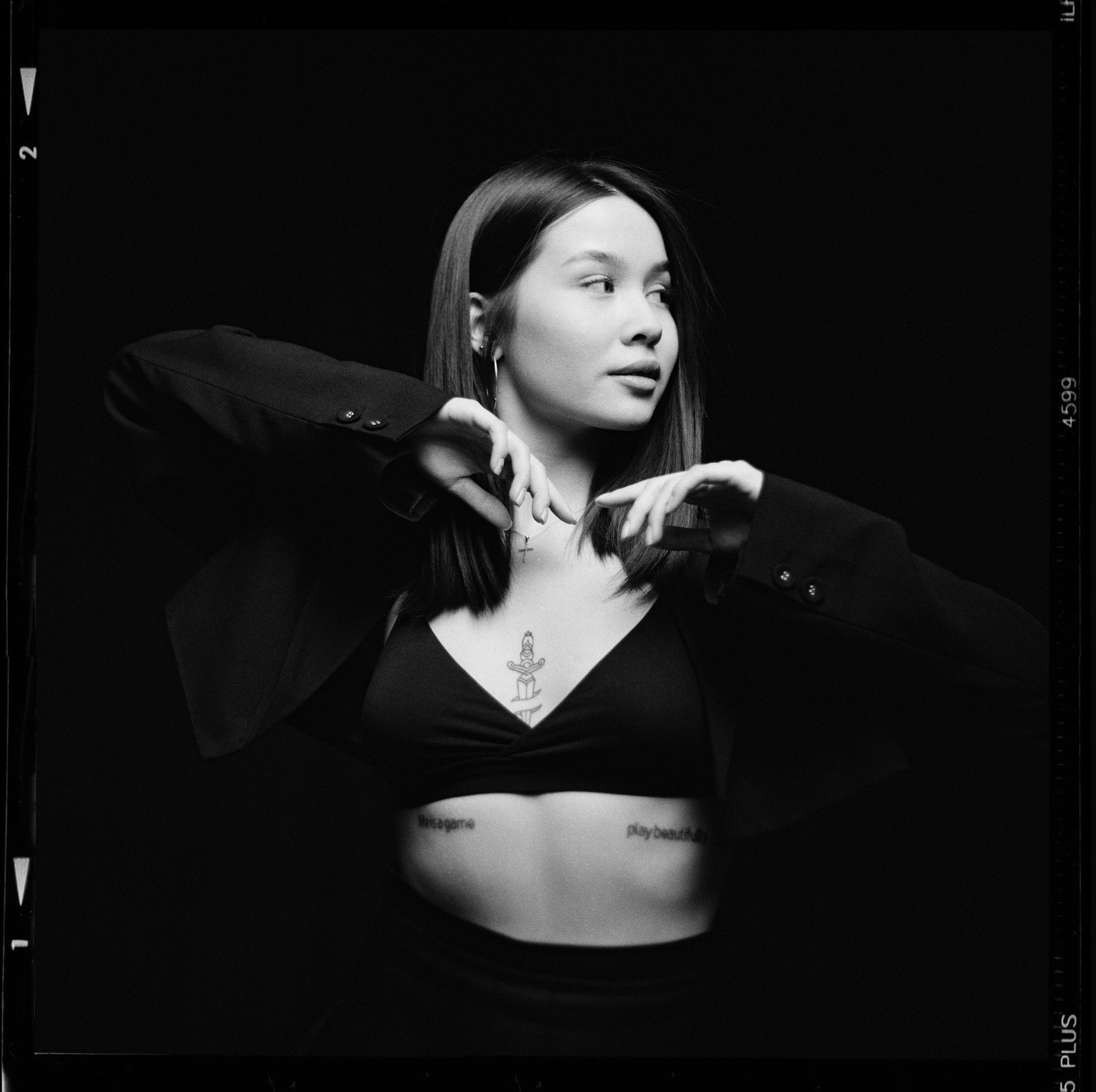 Красивая девушка азиатской внешности в черном пиджаке и белье на черном фоне смотрит вправо в фотостудии