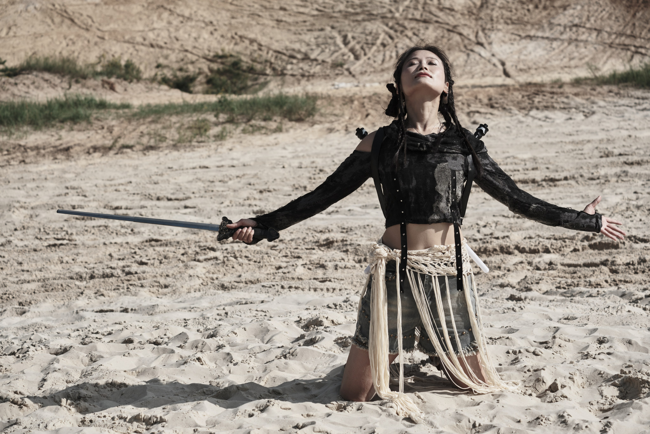 Девушка азиатской внешности с катаной в руке разводя руками смотрит в небо