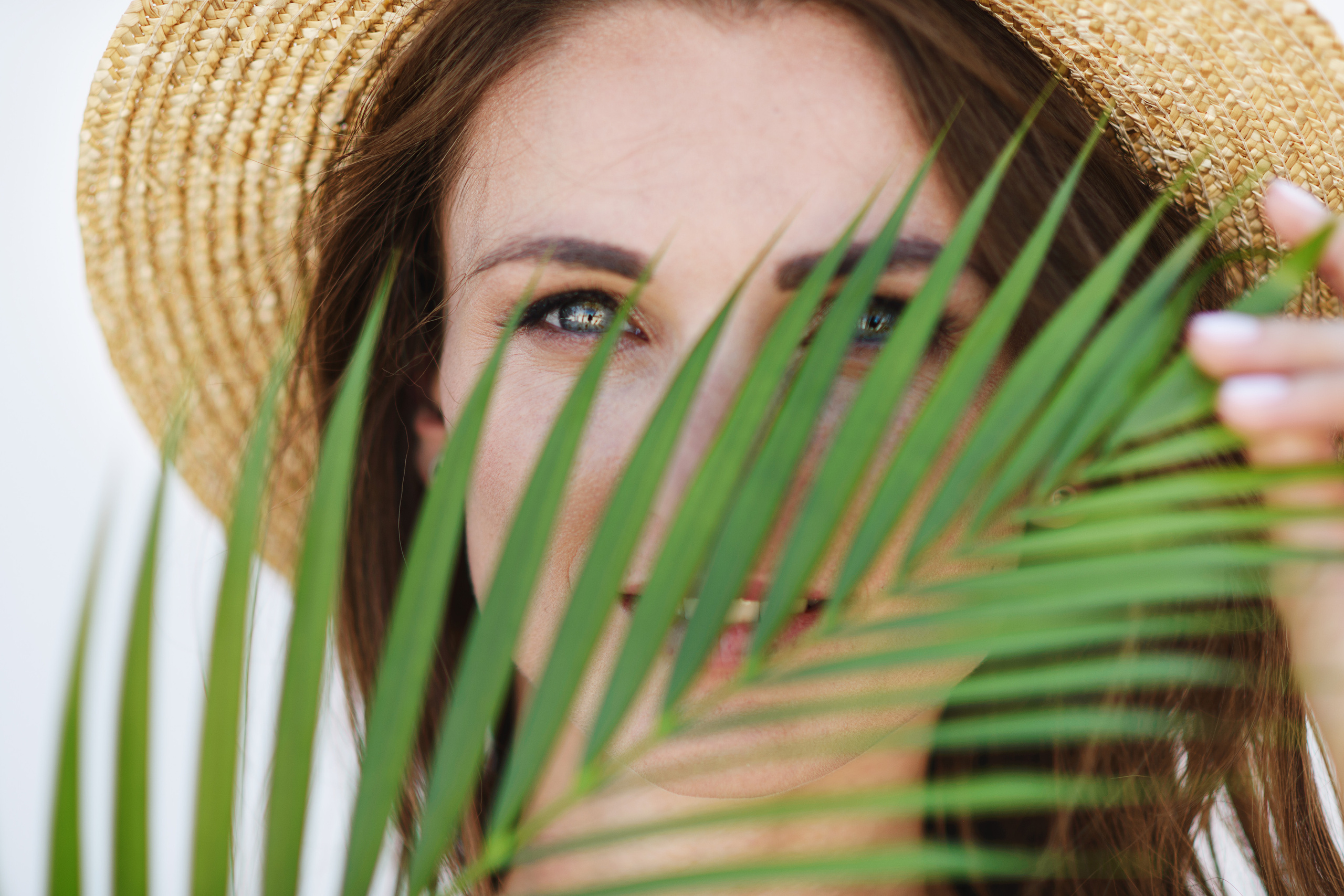 Портрет девушки в соломенной шляпе за пальмовым листом крупным планом