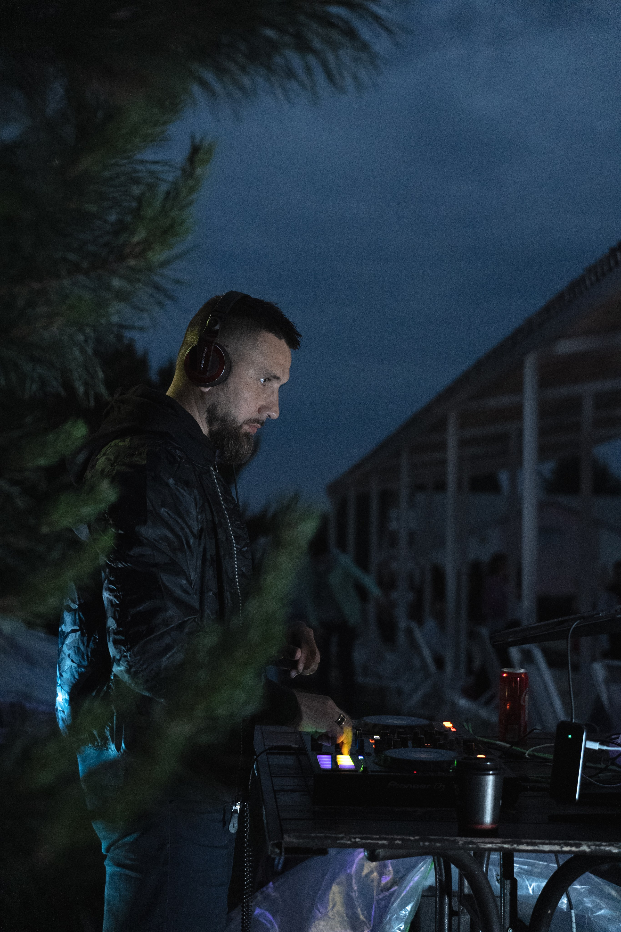 Диджей работает на пульте ночью на открытом воздухе с наушниками и светомузыкой