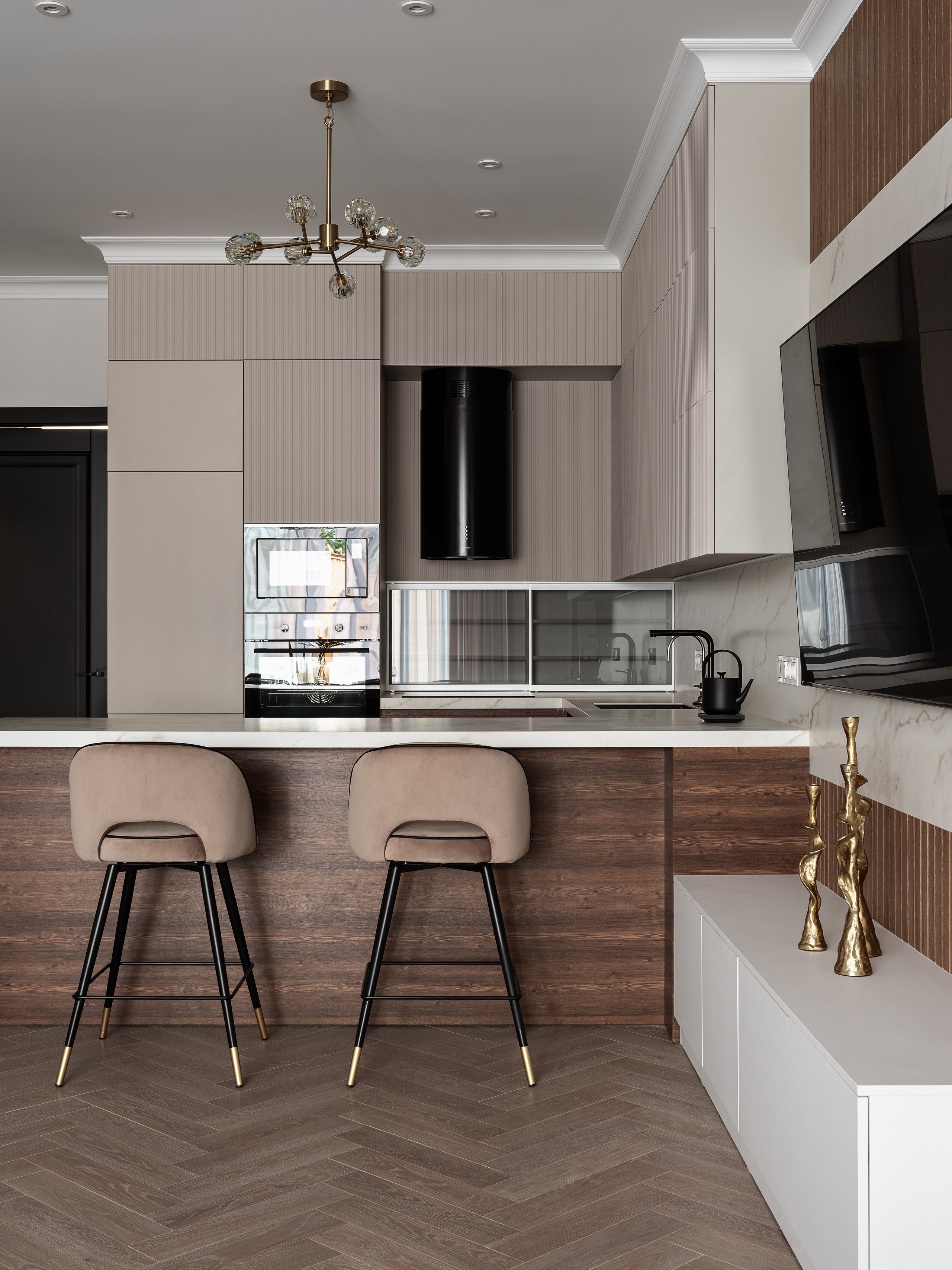 Современная кухня с барной стойкой из темного дерева и белой столешницей, барные стулья с мягкой обивкой и золотыми акцентами. Черная техника гармонично встроена, проект Василиссы Бачевой, стилист Наталья Якушева, фото Сергей Денисенко.